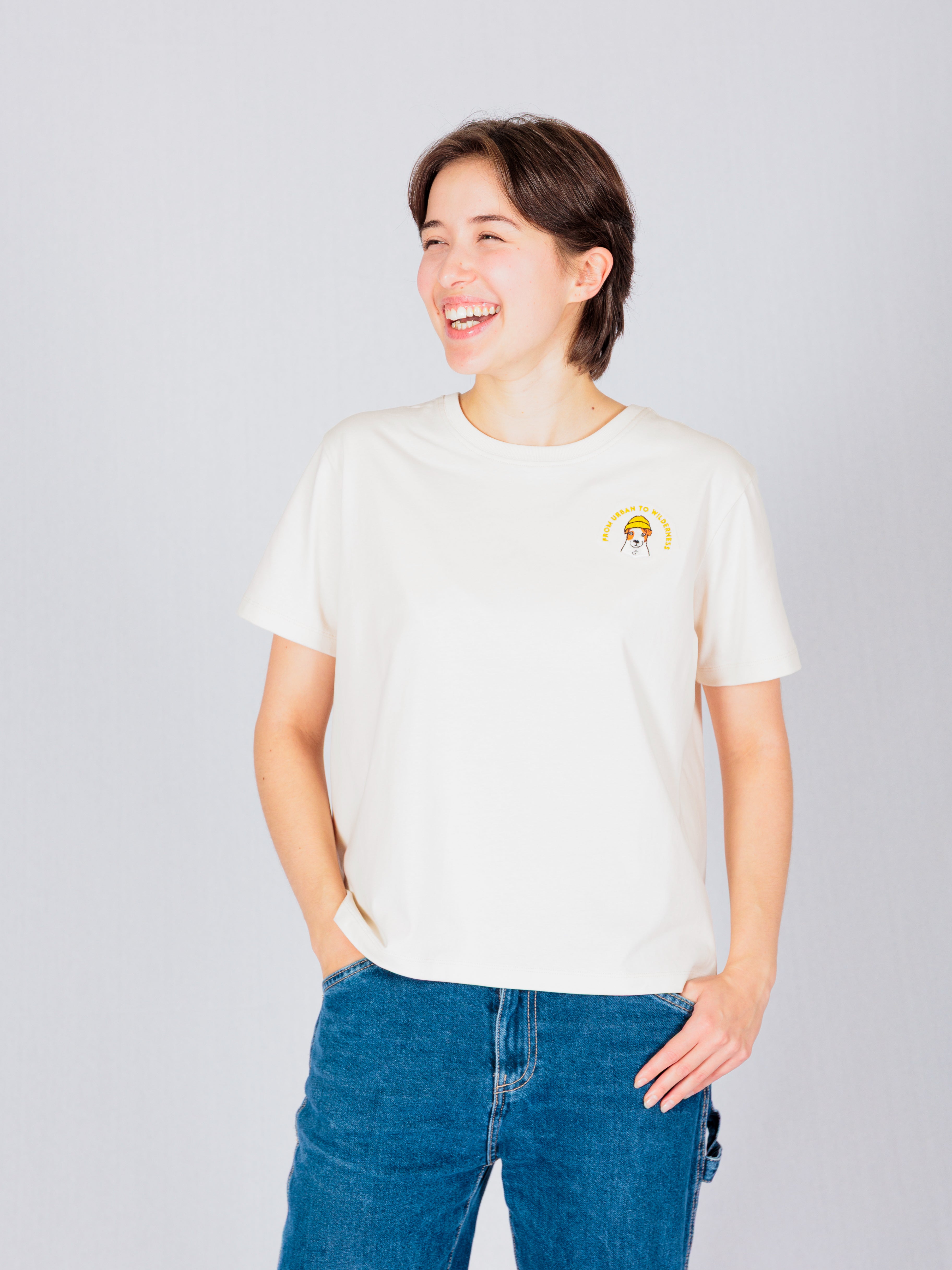 A person in a white t-shirt and jeans smiles, standing against a plain light background.