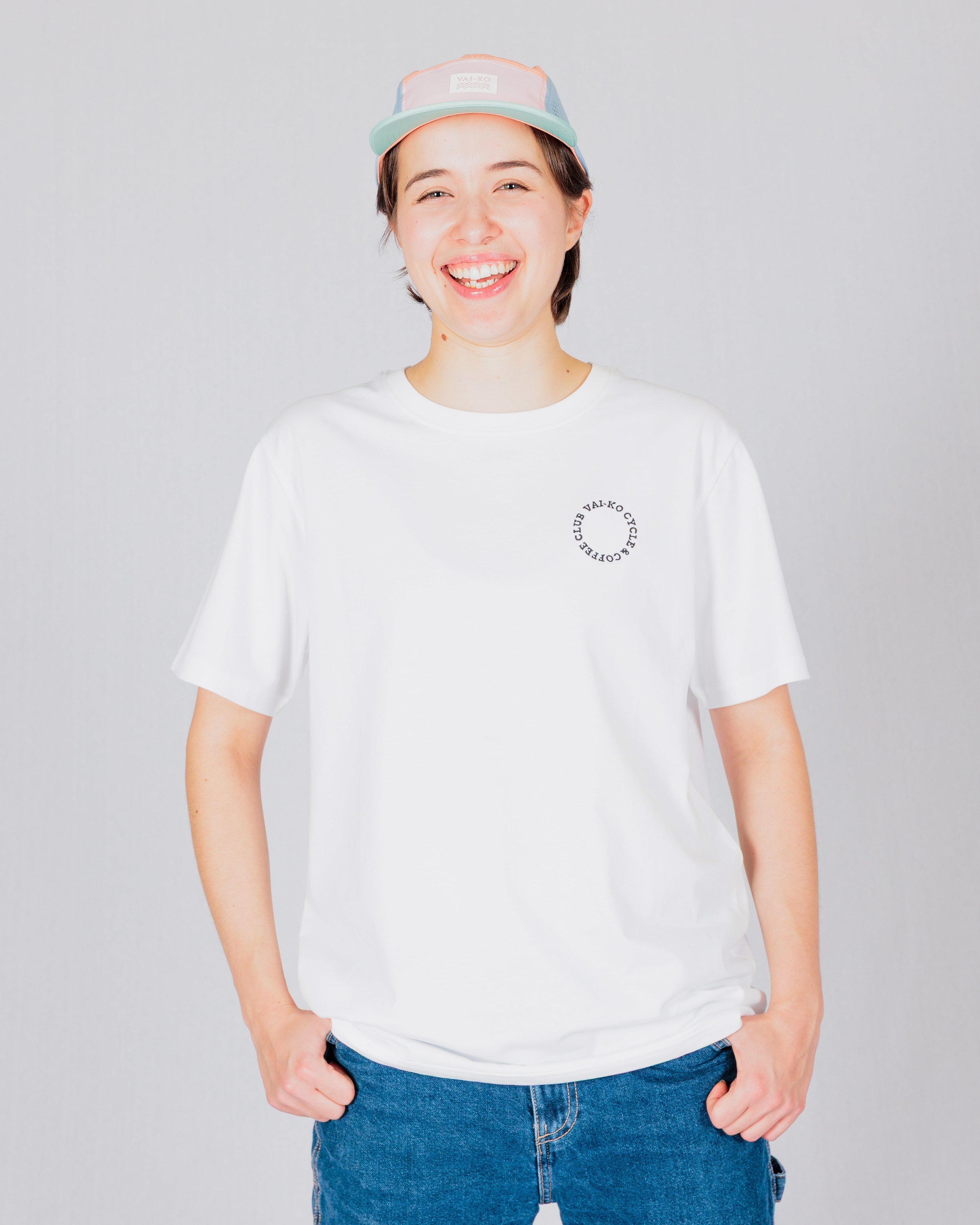 Person in a white t-shirt and pastel cap smiling, standing against a light gray background.