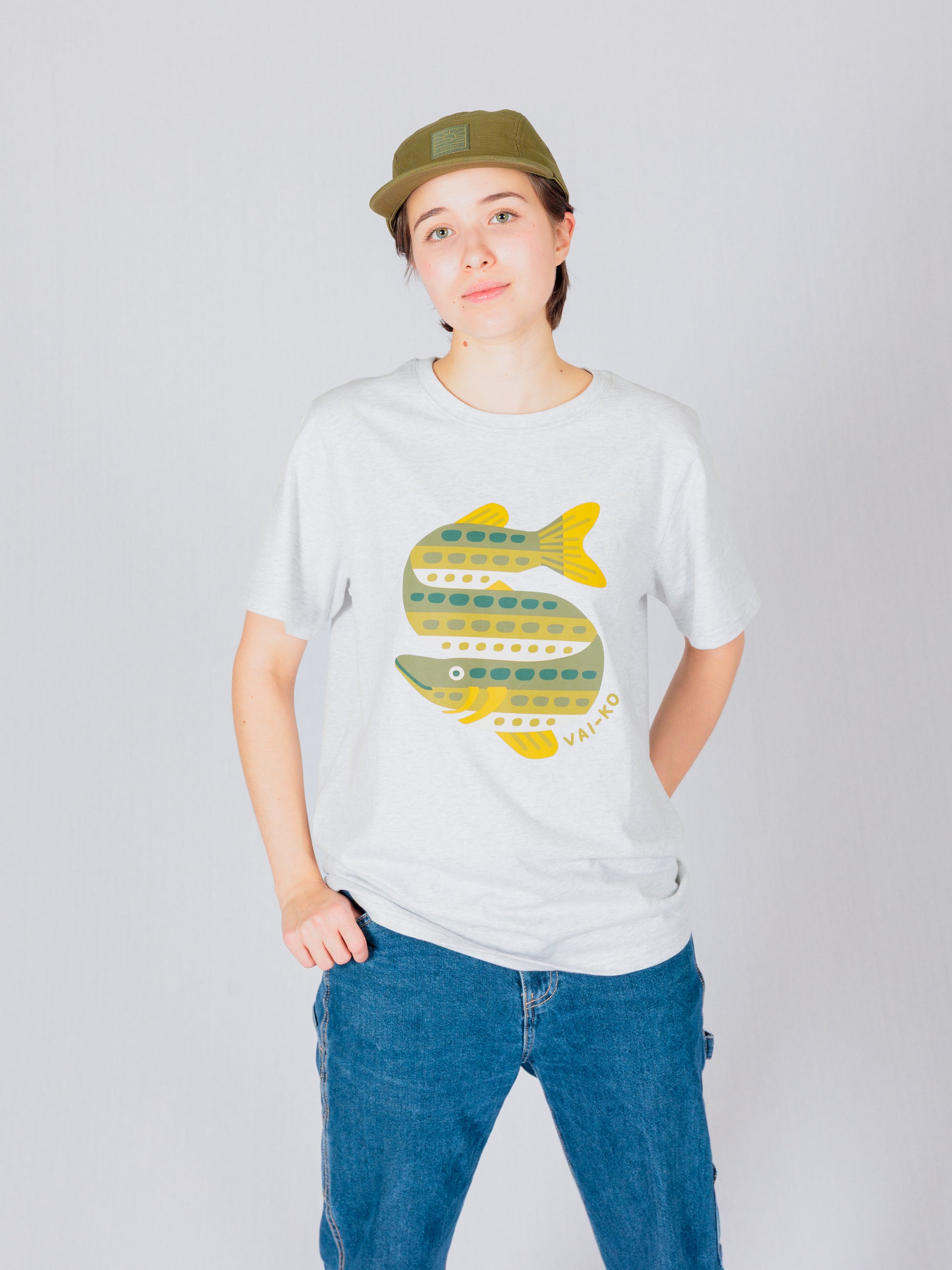 Person in a cap and jeans wearing a light t-shirt with a colorful fish illustration on the front.