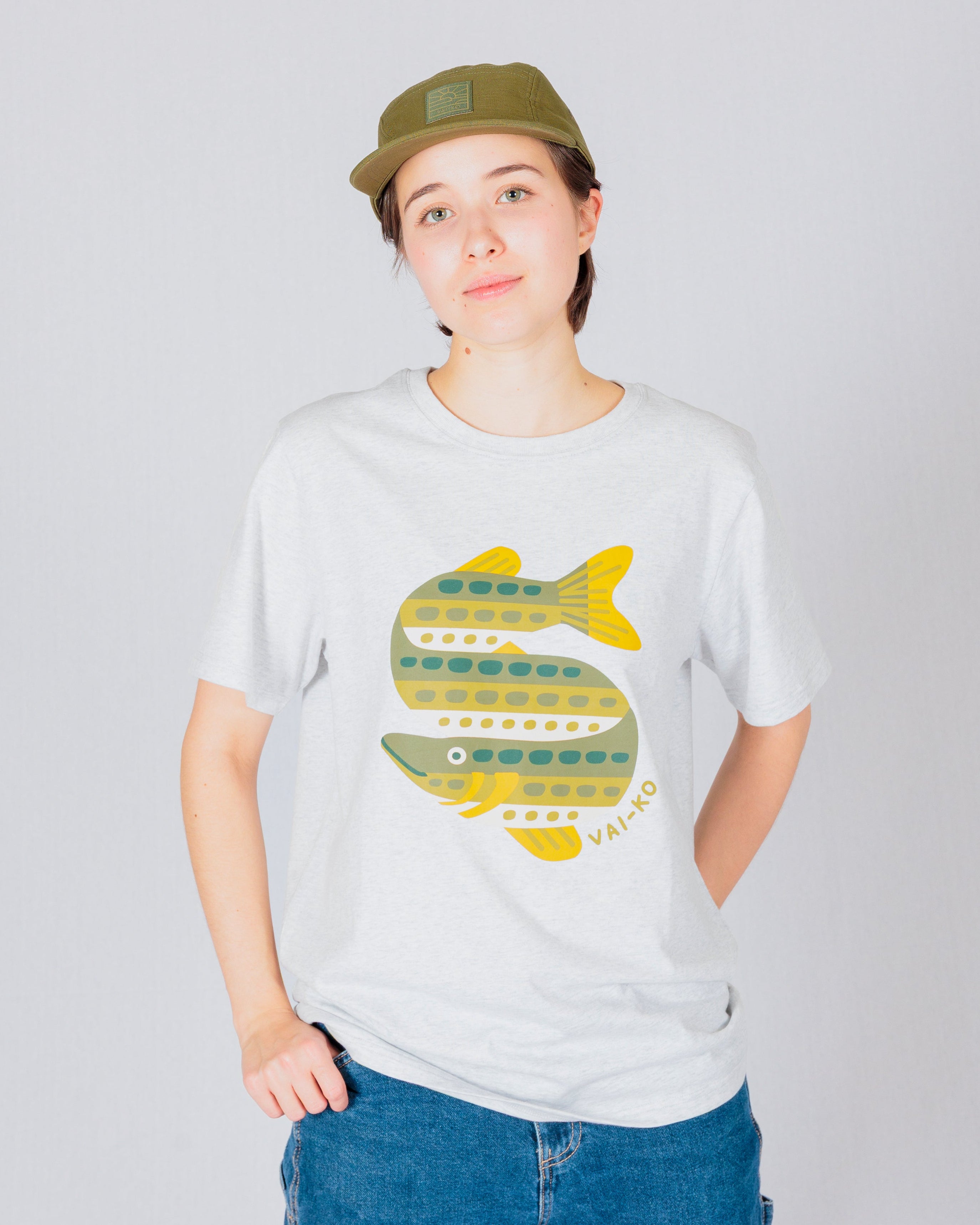 Person in a cap and jeans wearing a light t-shirt with a colorful fish illustration on the front.