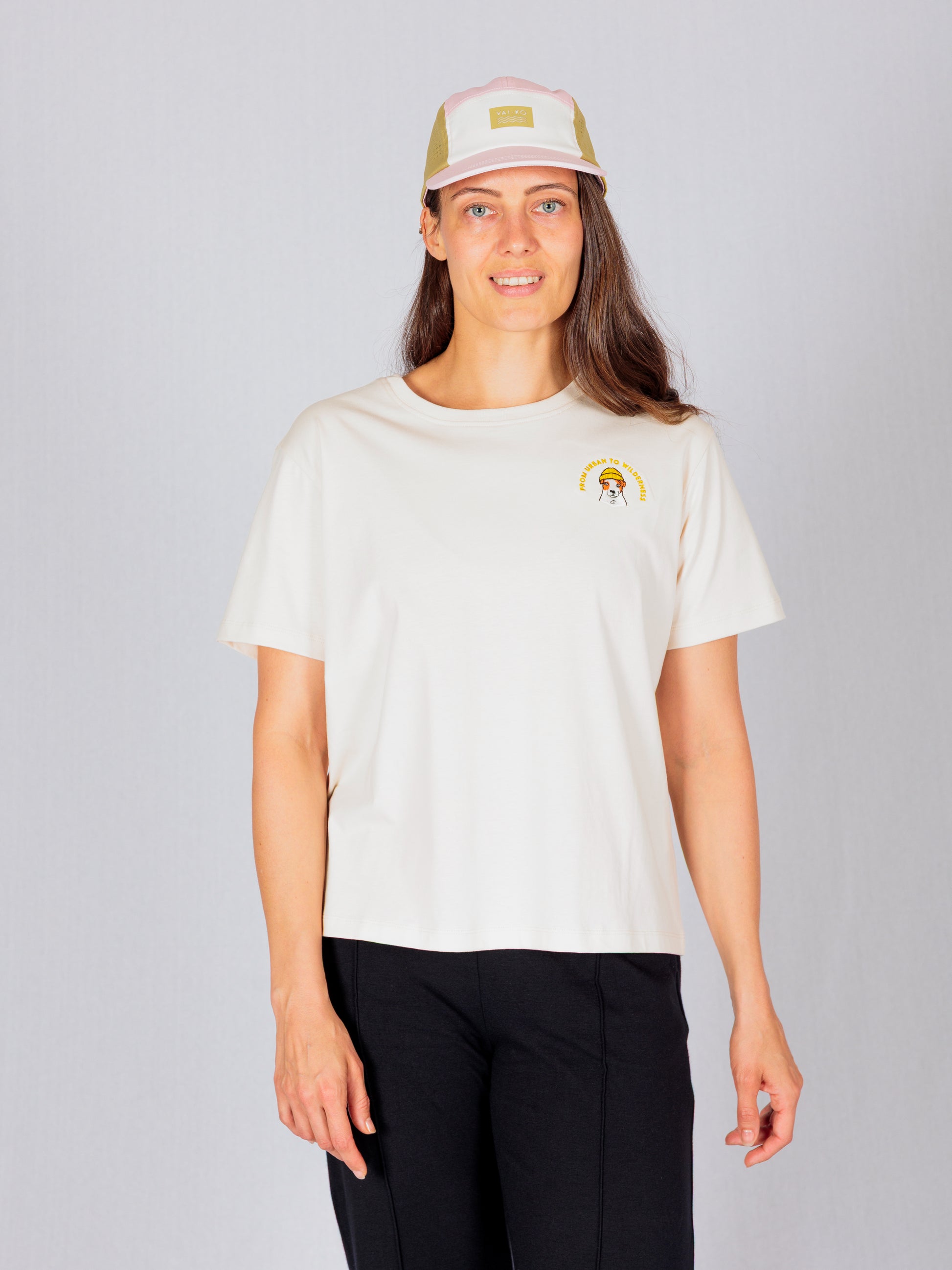 Woman in a light t-shirt and cap standing and smiling against a plain light gray background.