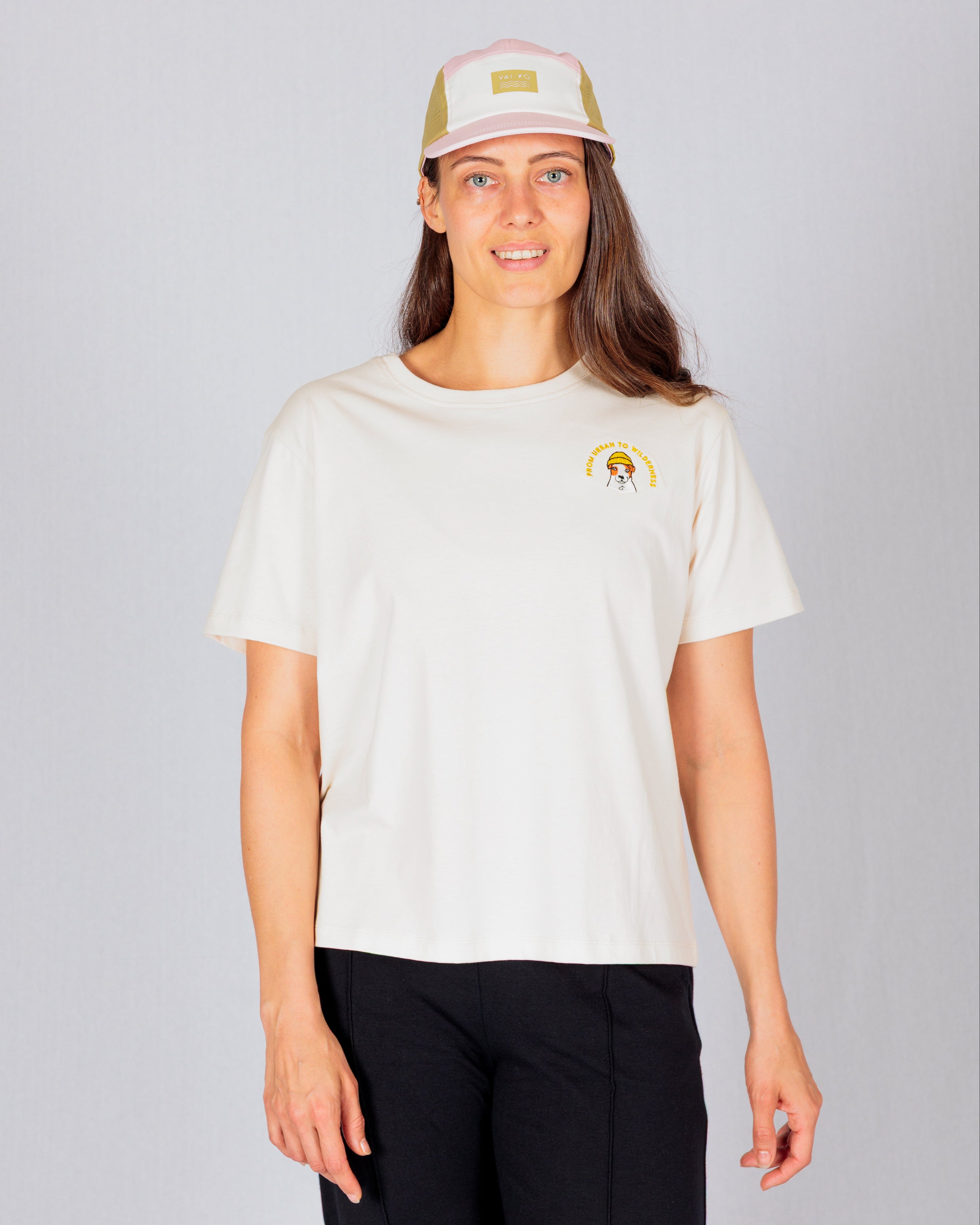 Woman in a light t-shirt and cap standing and smiling against a plain light gray background.