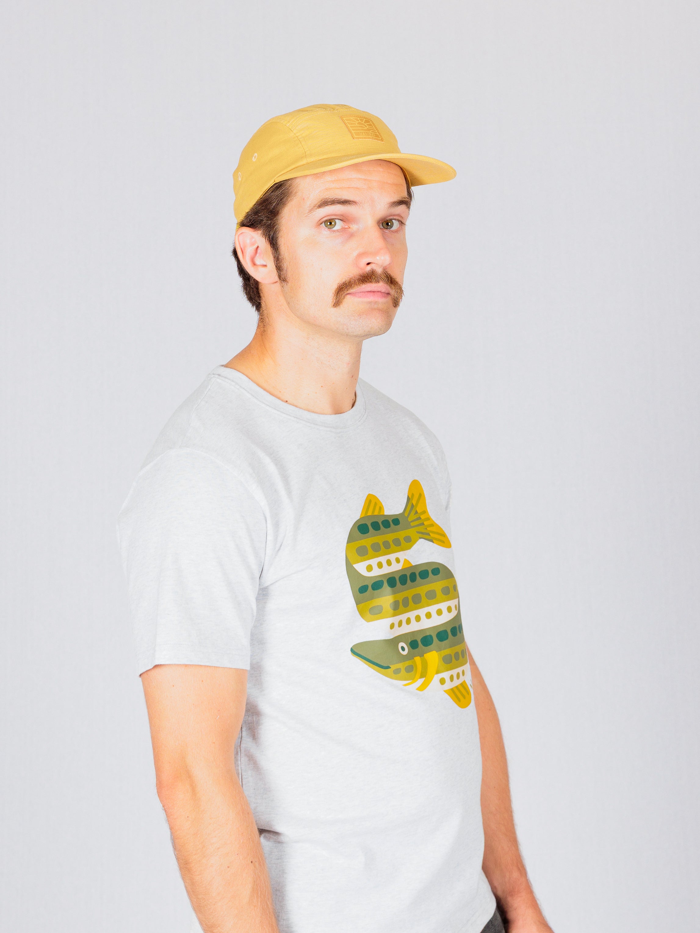 Man in a yellow cap and fish-print t-shirt standing against a plain light background, looking at the camera.