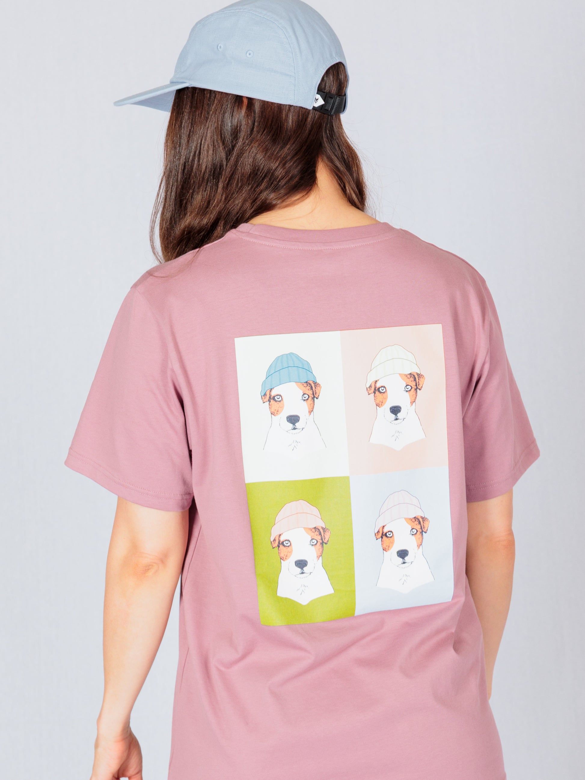 Person in a pink shirt and cap; shirt has four colorful dog illustrations wearing beanies on the back.