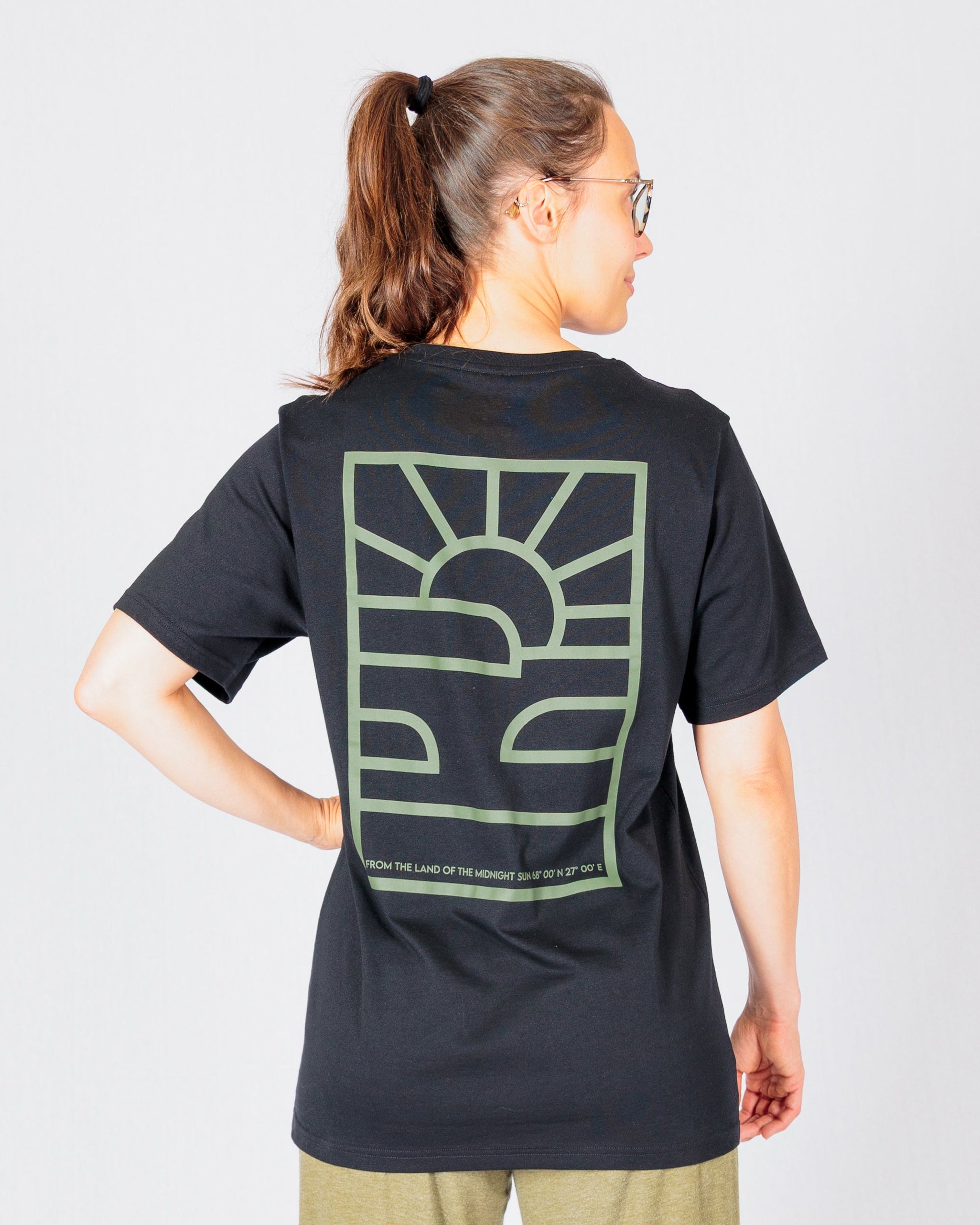 Person facing away, wearing a black t-shirt with a green abstract sun and waves design on the back.