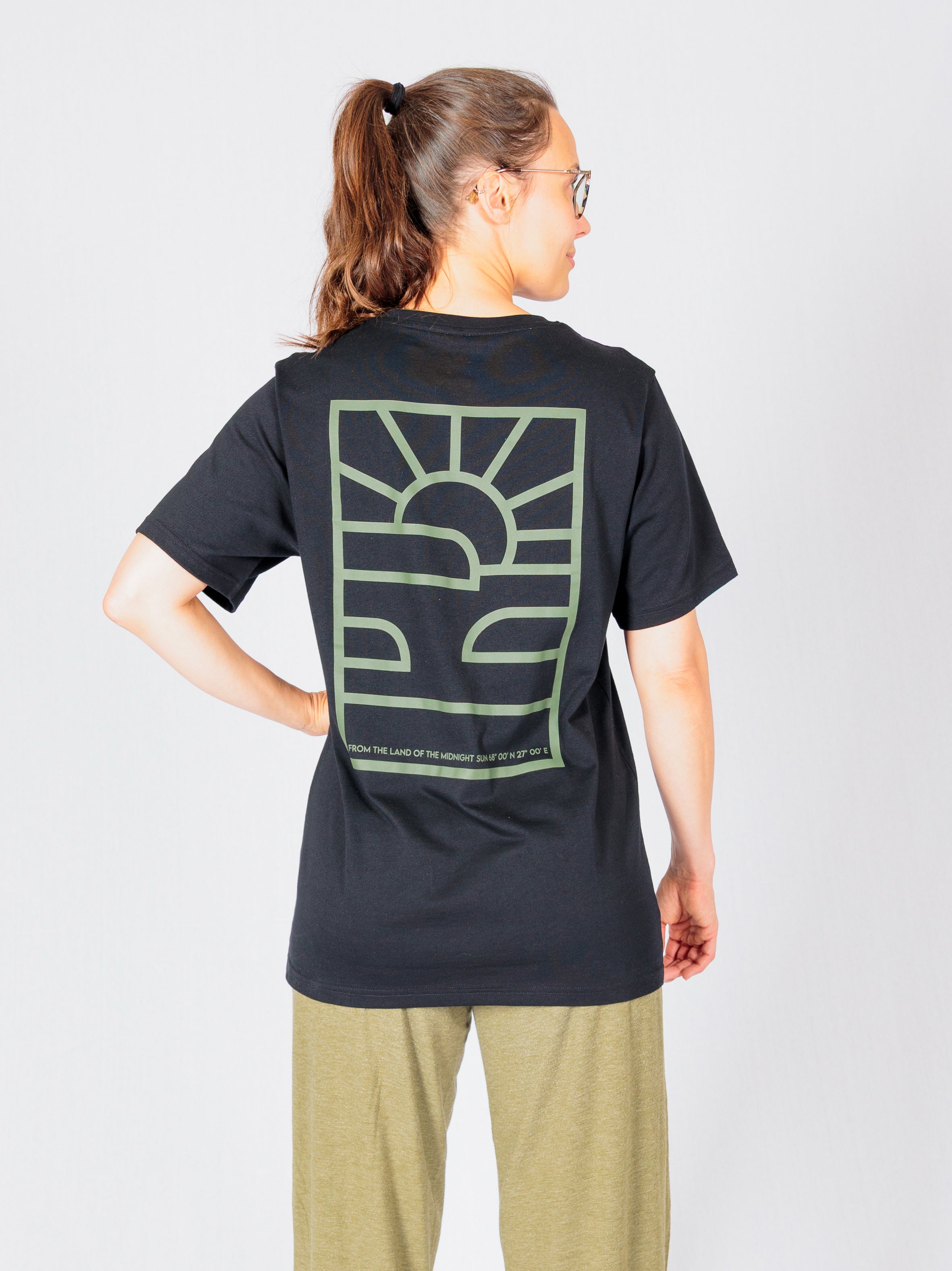 Person facing away, wearing a black t-shirt with a green abstract sun and waves design on the back.