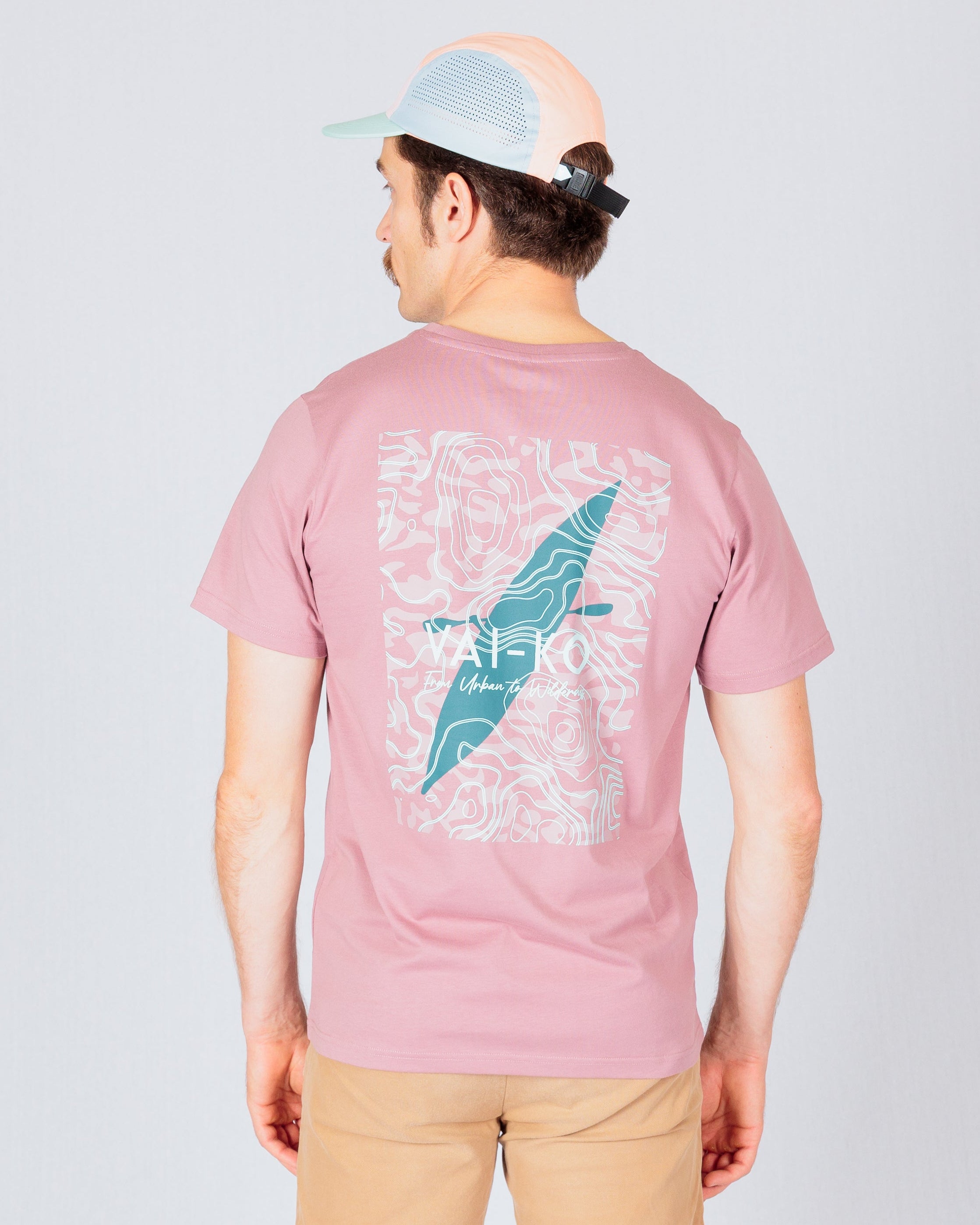Man wearing a pink graphic T-shirt and beige pants, facing away, with a cap on his head.
