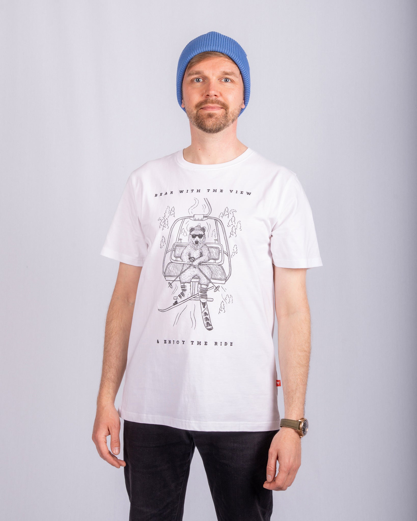 Man in a blue beanie and white graphic t-shirt standing against a plain light background.
