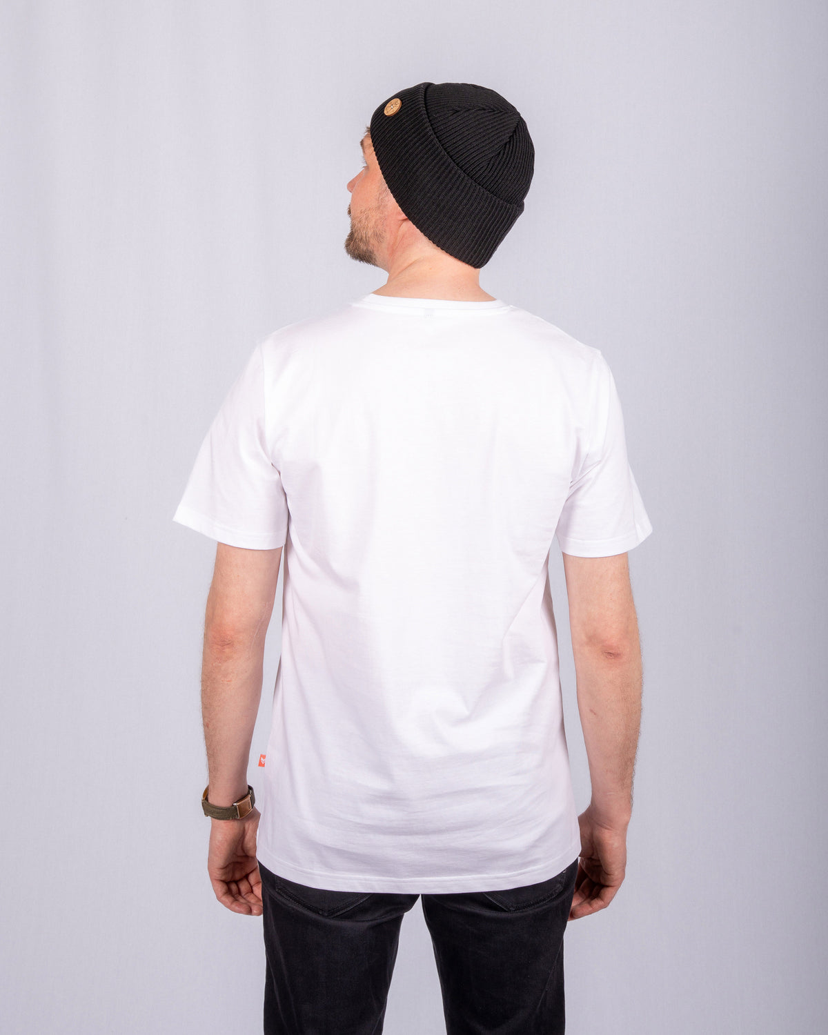 Man in a white t-shirt and black beanie, standing with his back to the camera against a plain background.