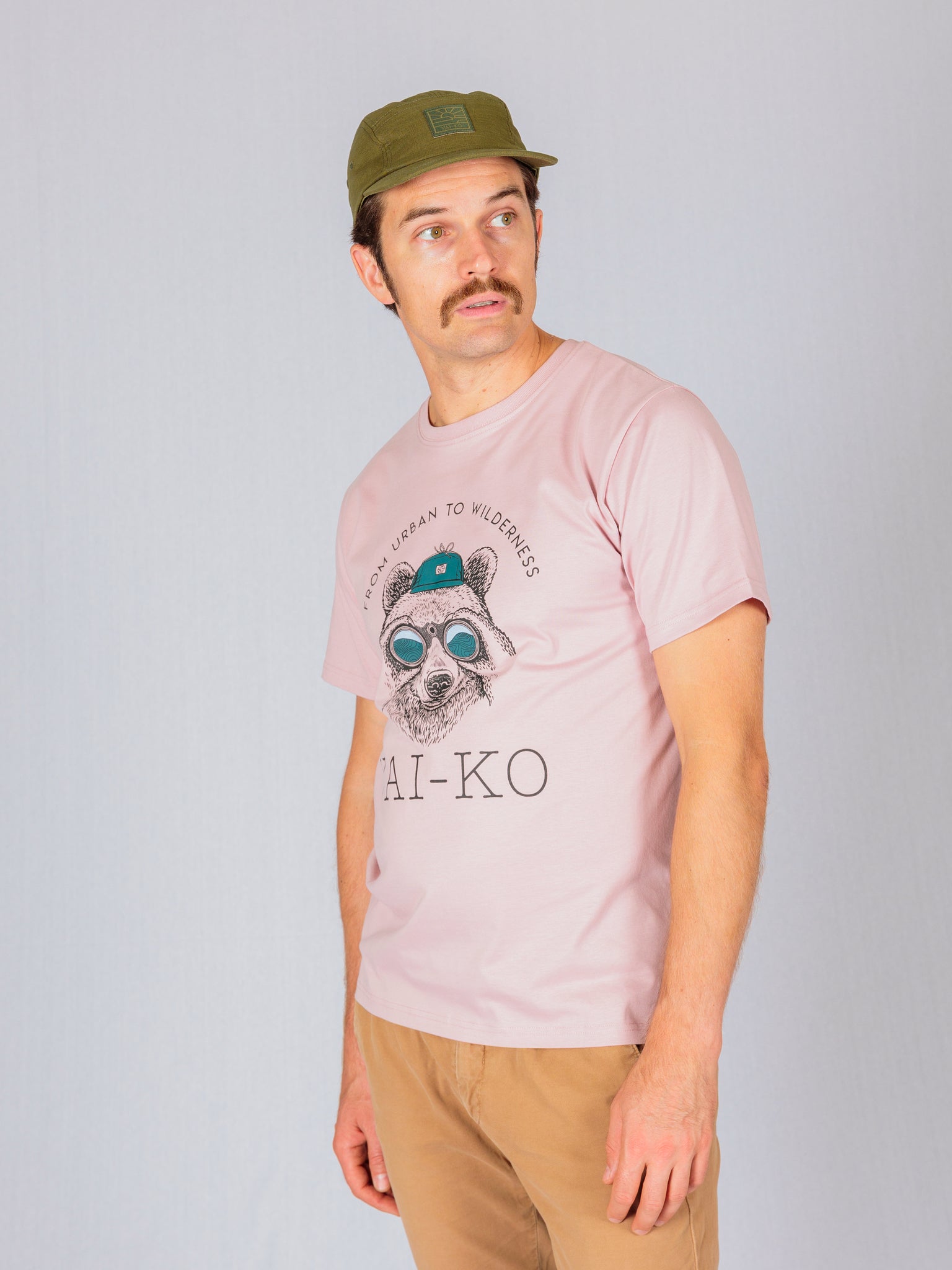 Man in a green cap and pink graphic T-shirt with a raccoon design, looking to the side.