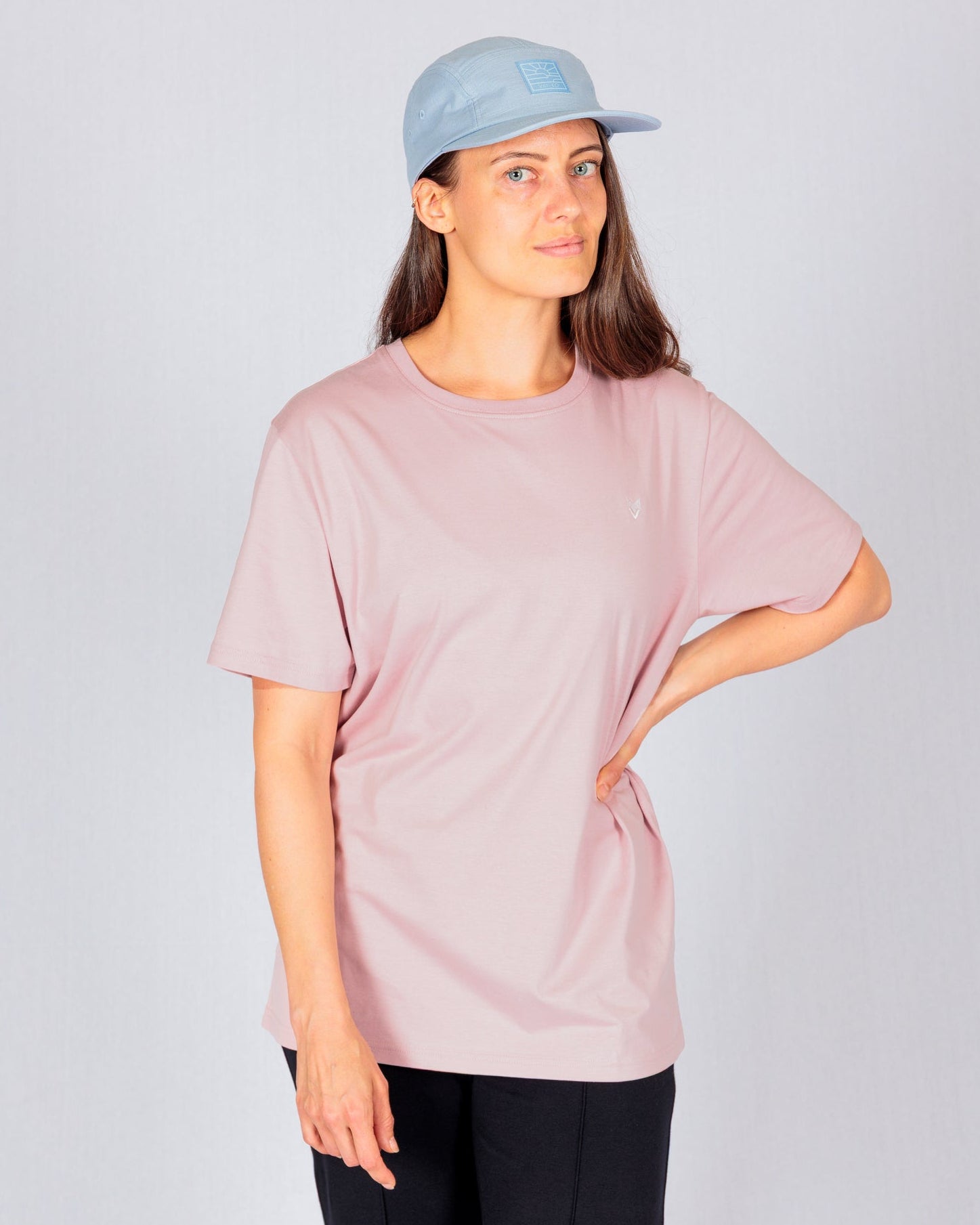 Woman wearing a light blue cap, pink t-shirt, and black pants, standing with one hand on her hip.