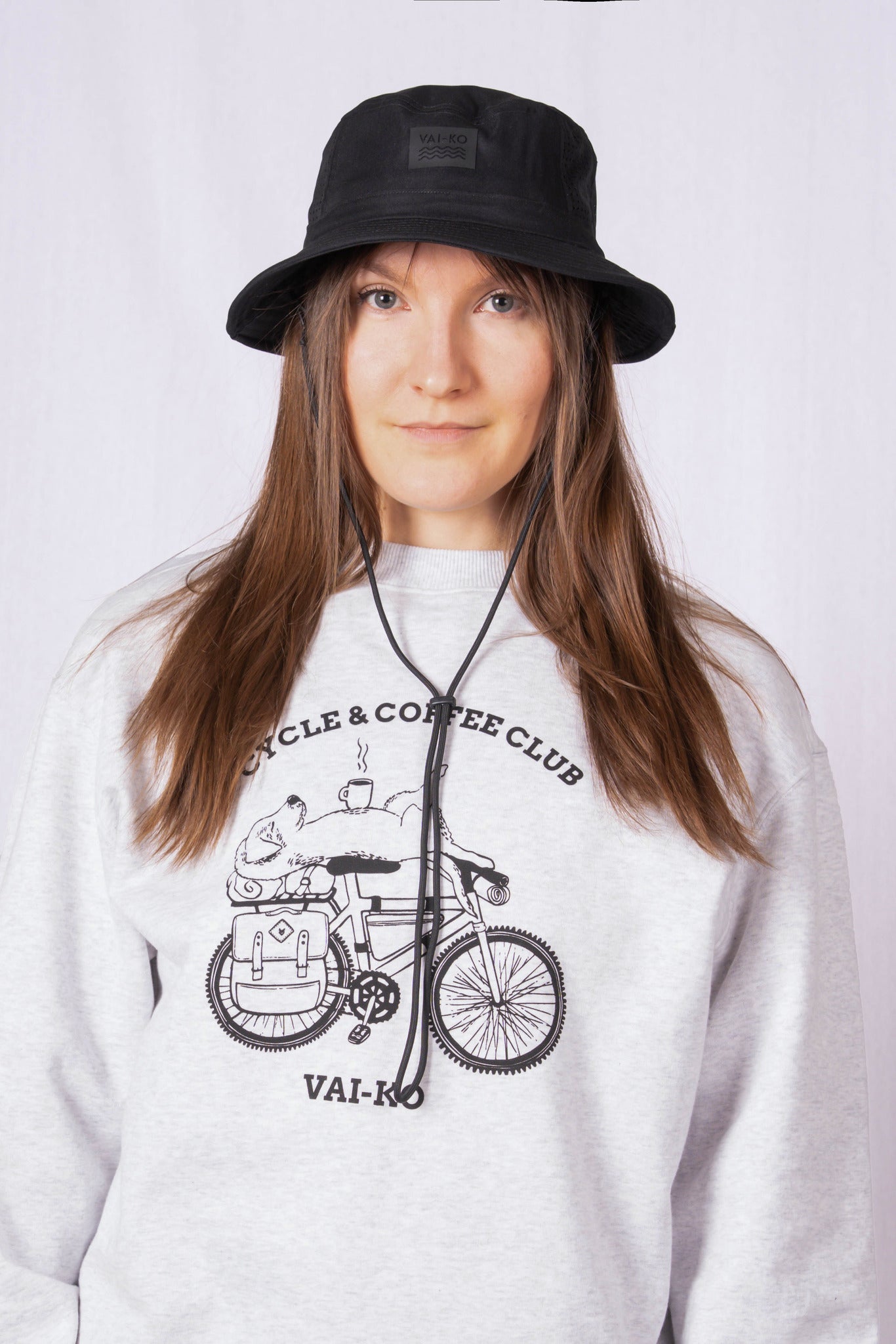 Woman in a black bucket hat and a gray sweatshirt with a bicycle and coffee club graphic, facing forward.