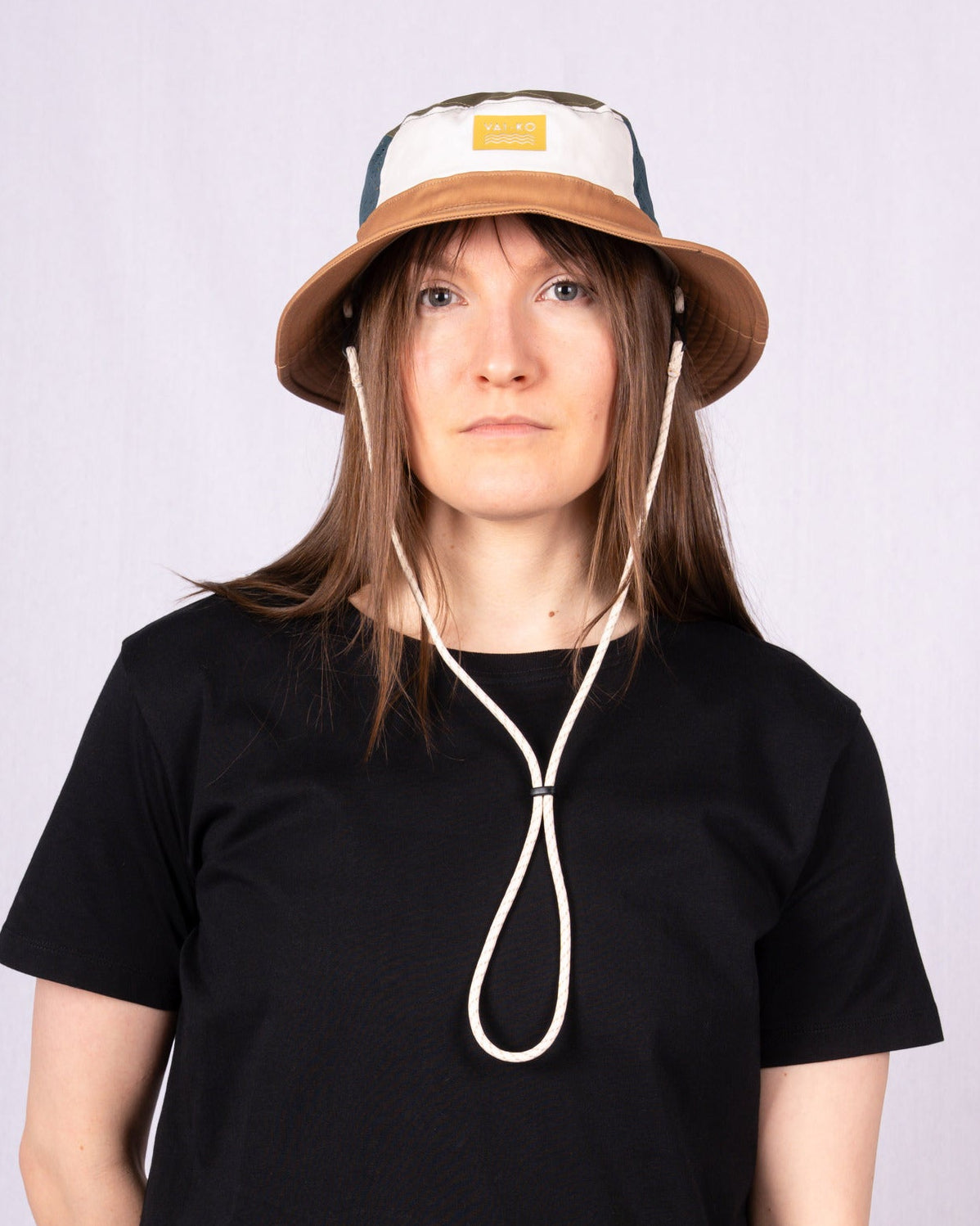 Person wearing a black t-shirt and a beige bucket hat with chin straps, standing against a plain background.