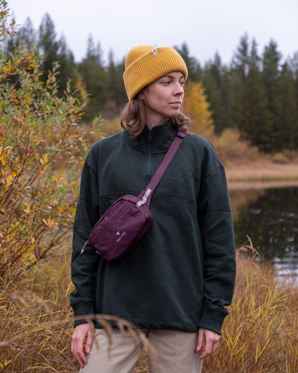 A person in a yellow beanie and dark green sweatshirt wearing a purple crossbody bag.