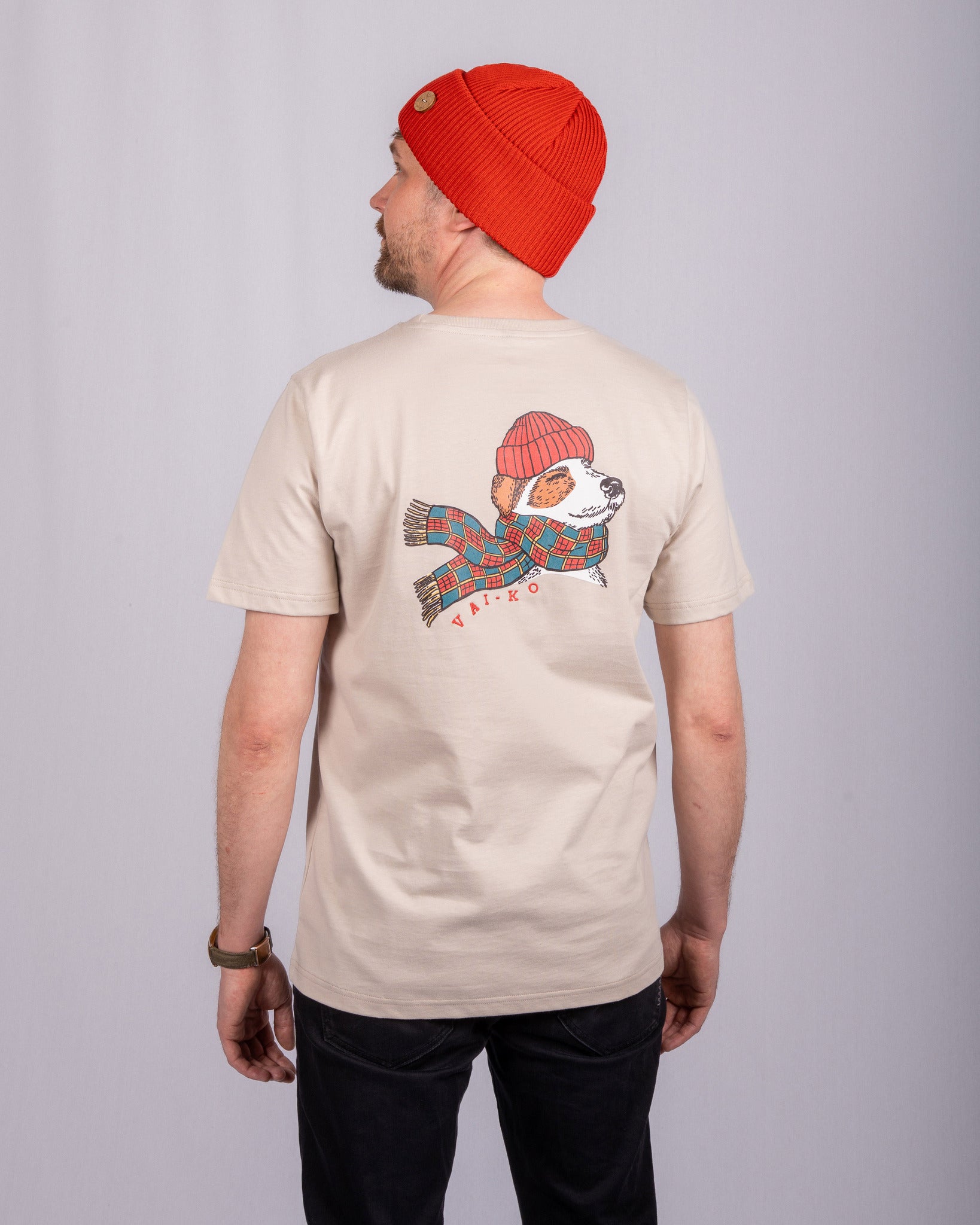 A man in a red beanie and beige T-shirt with a dog in a hat and scarf design on the back.