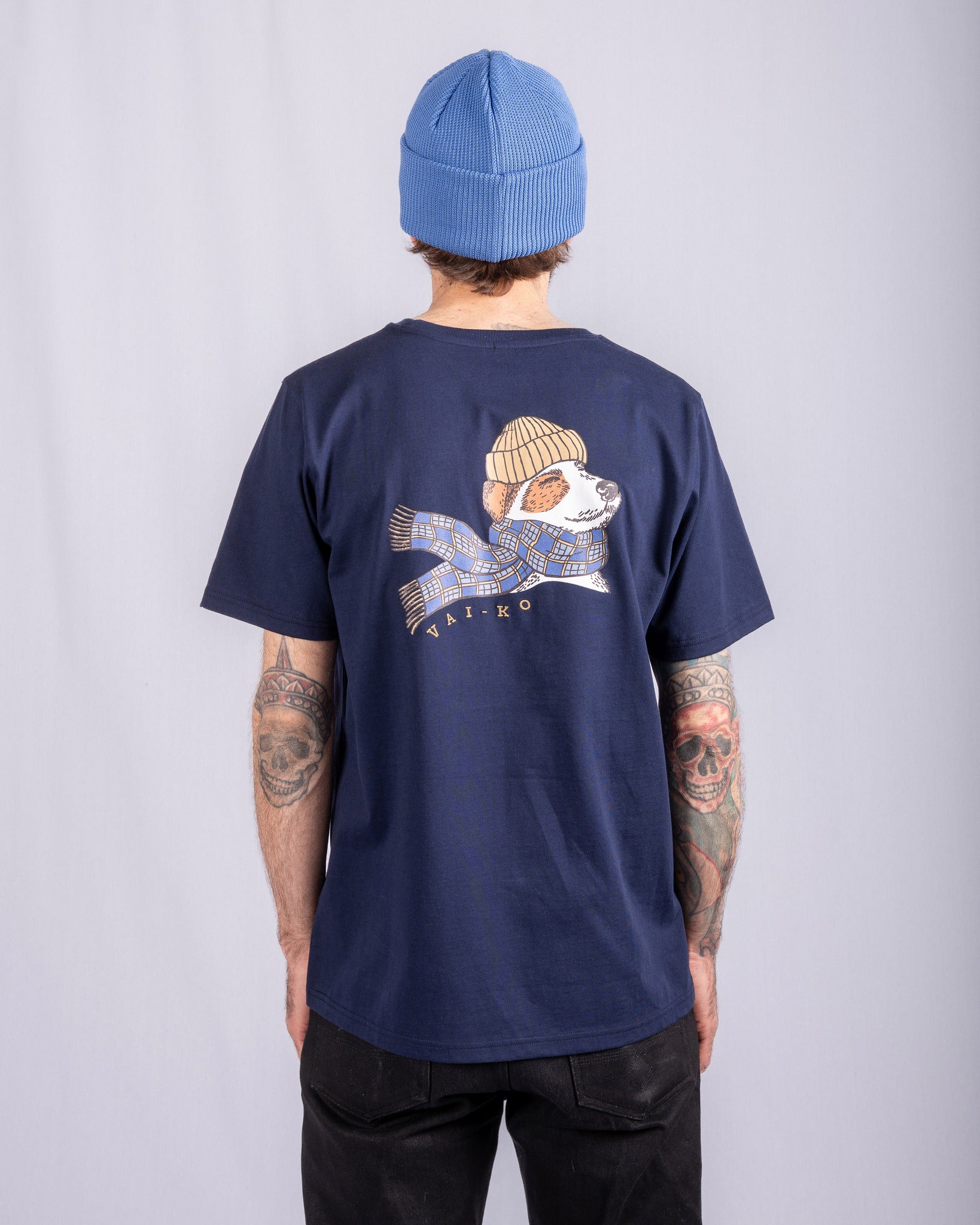 Person in blue beanie and navy t-shirt with dog graphic; facing away from the camera; tattoos visible.