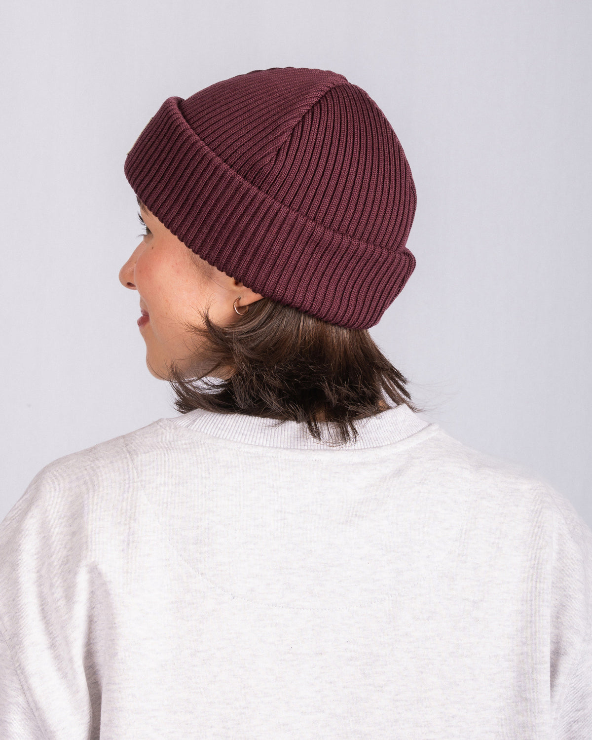Person in a maroon knit beanie and light sweater, seen from behind against a plain background.