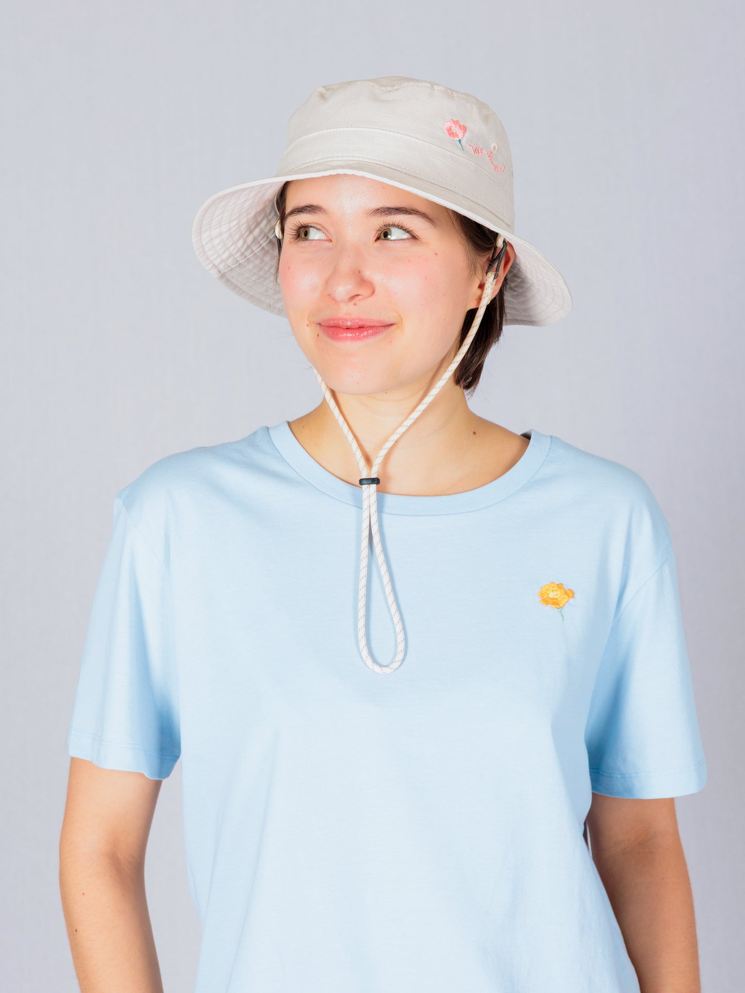Person in a light blue t-shirt and beige bucket hat smiling and looking to the side against a plain background.