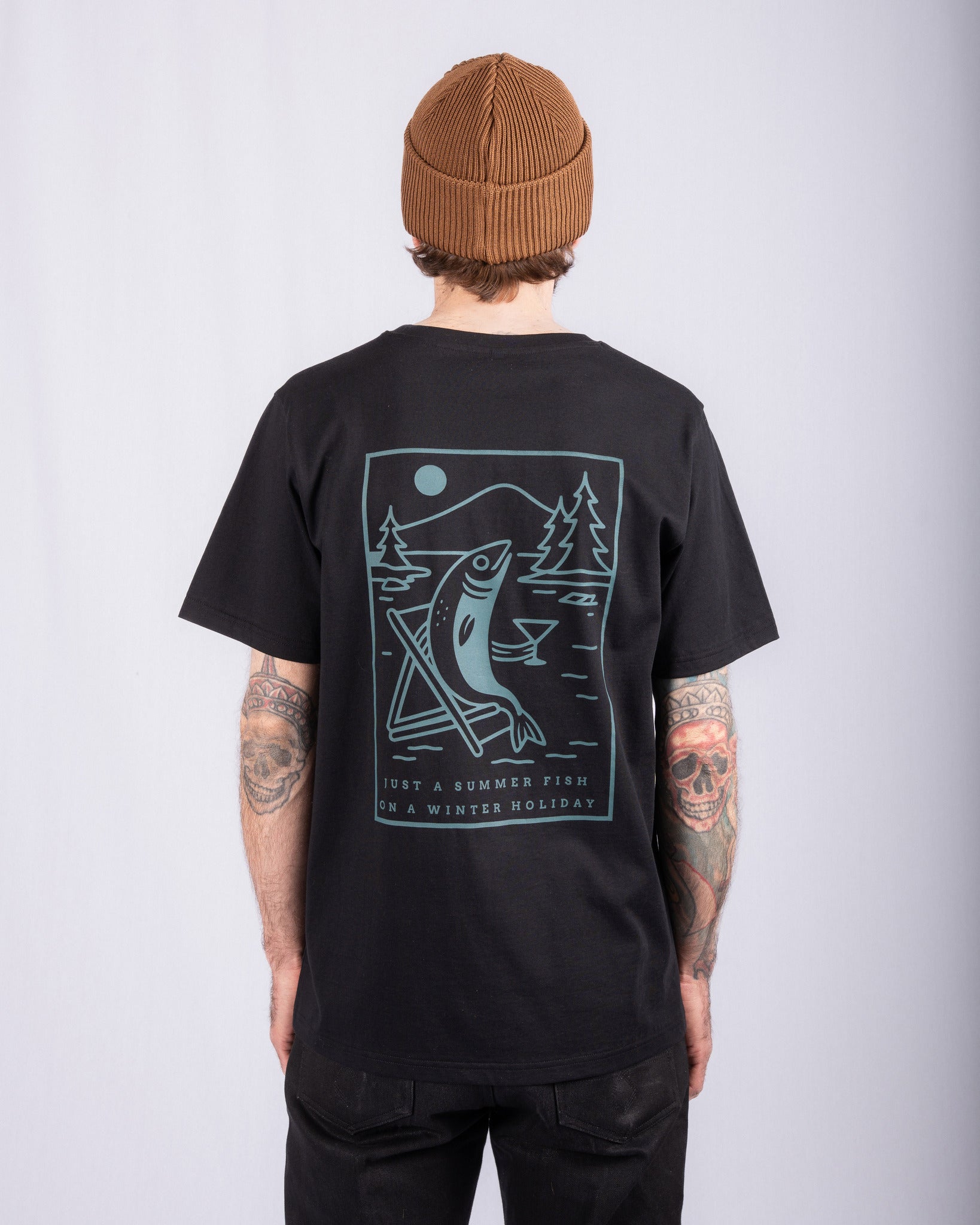 Person in a brown beanie, black shirt with fish graphic and text, seen from the back against light background.