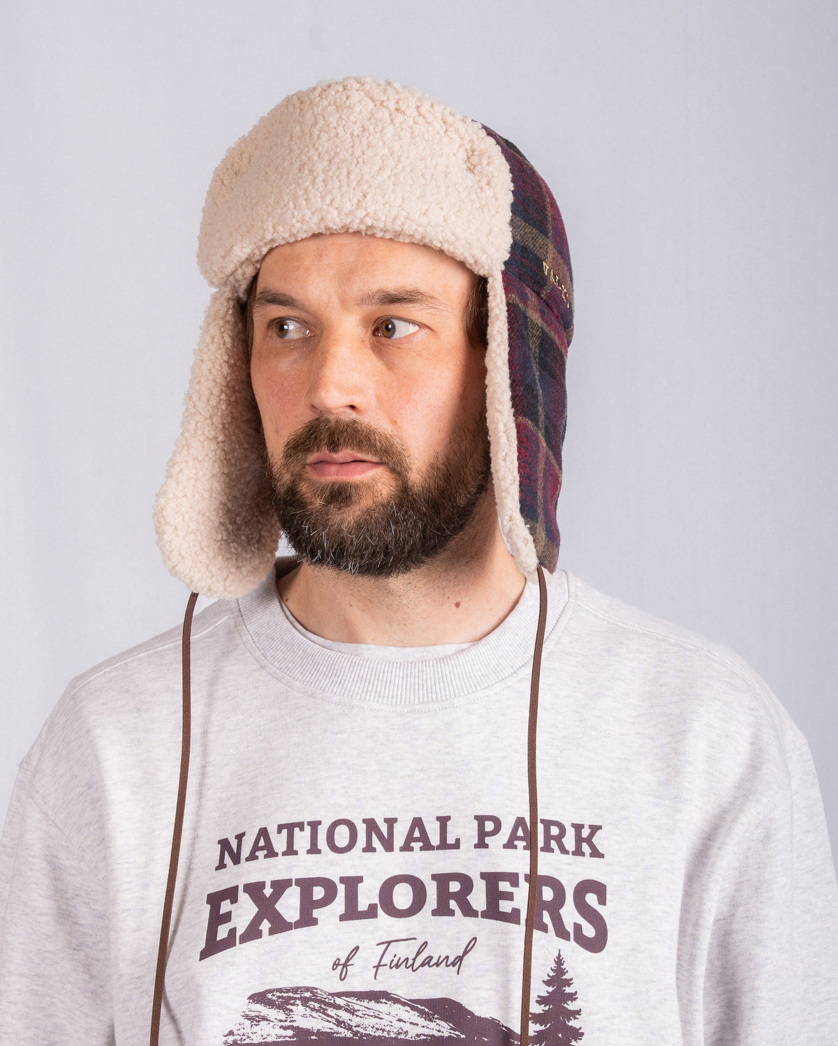 Bearded man in a trapper hat and National Park Explorers sweatshirt looking slightly to the side.
