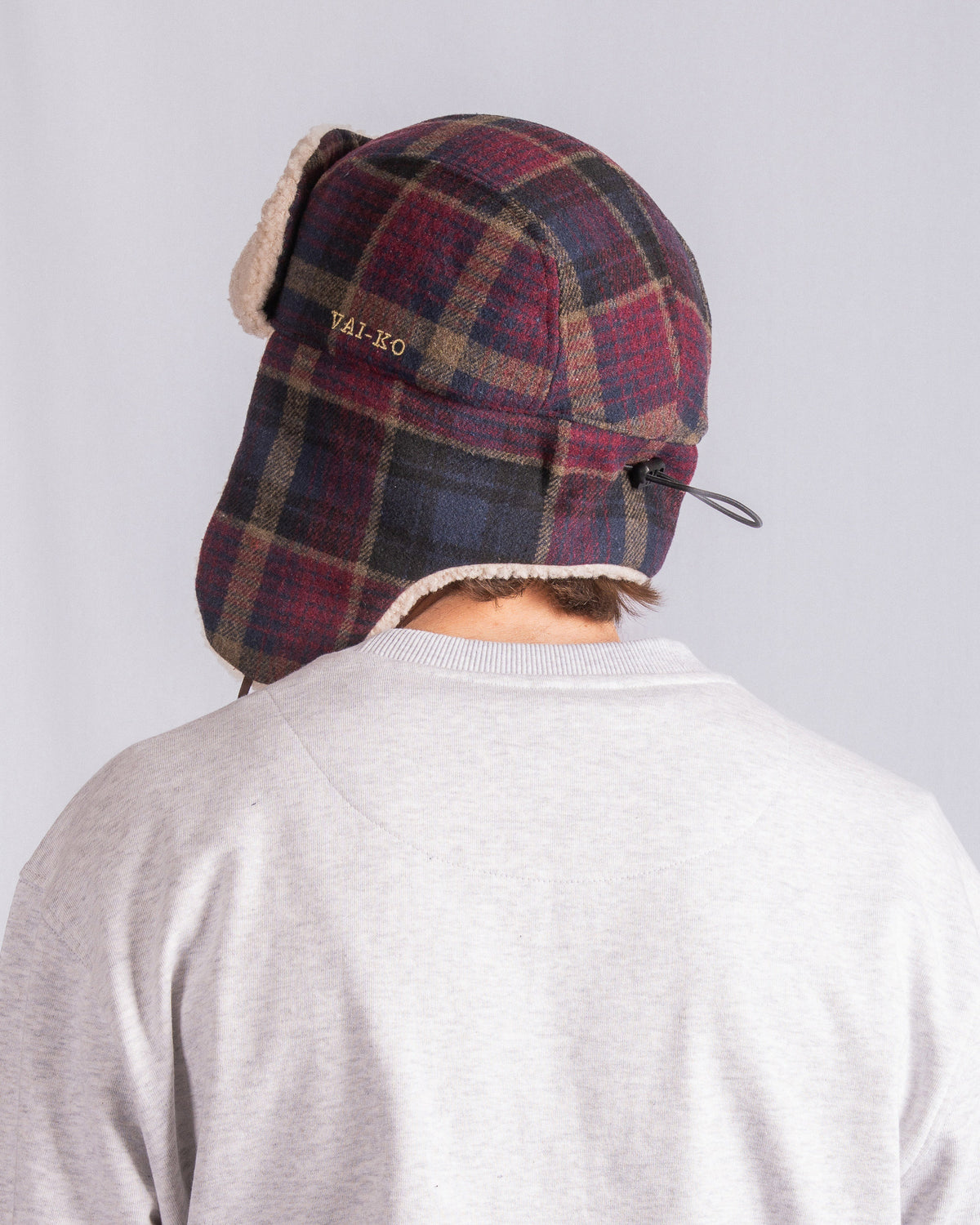 Person wearing a plaid winter hat and light gray shirt, seen from behind against a plain background.