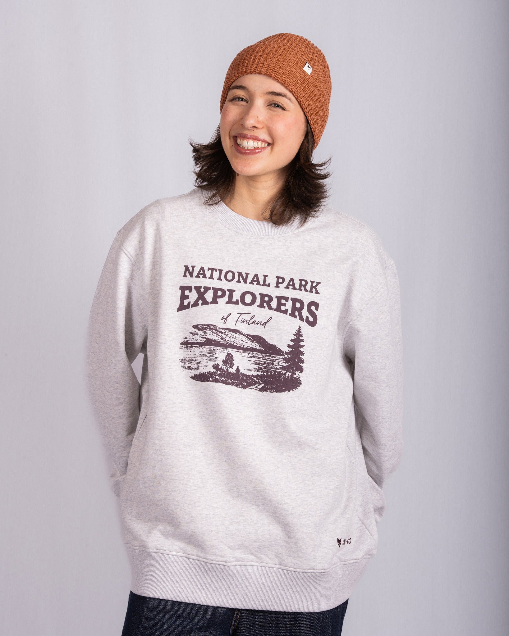 Smiling person in a tan beanie and gray National Park Explorers sweatshirt stands against a plain background.