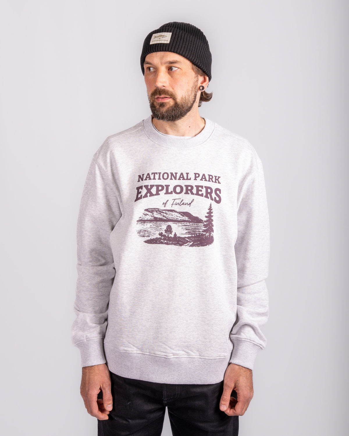 Man in a gray National Park Explorers sweatshirt and black beanie standing against a plain background.