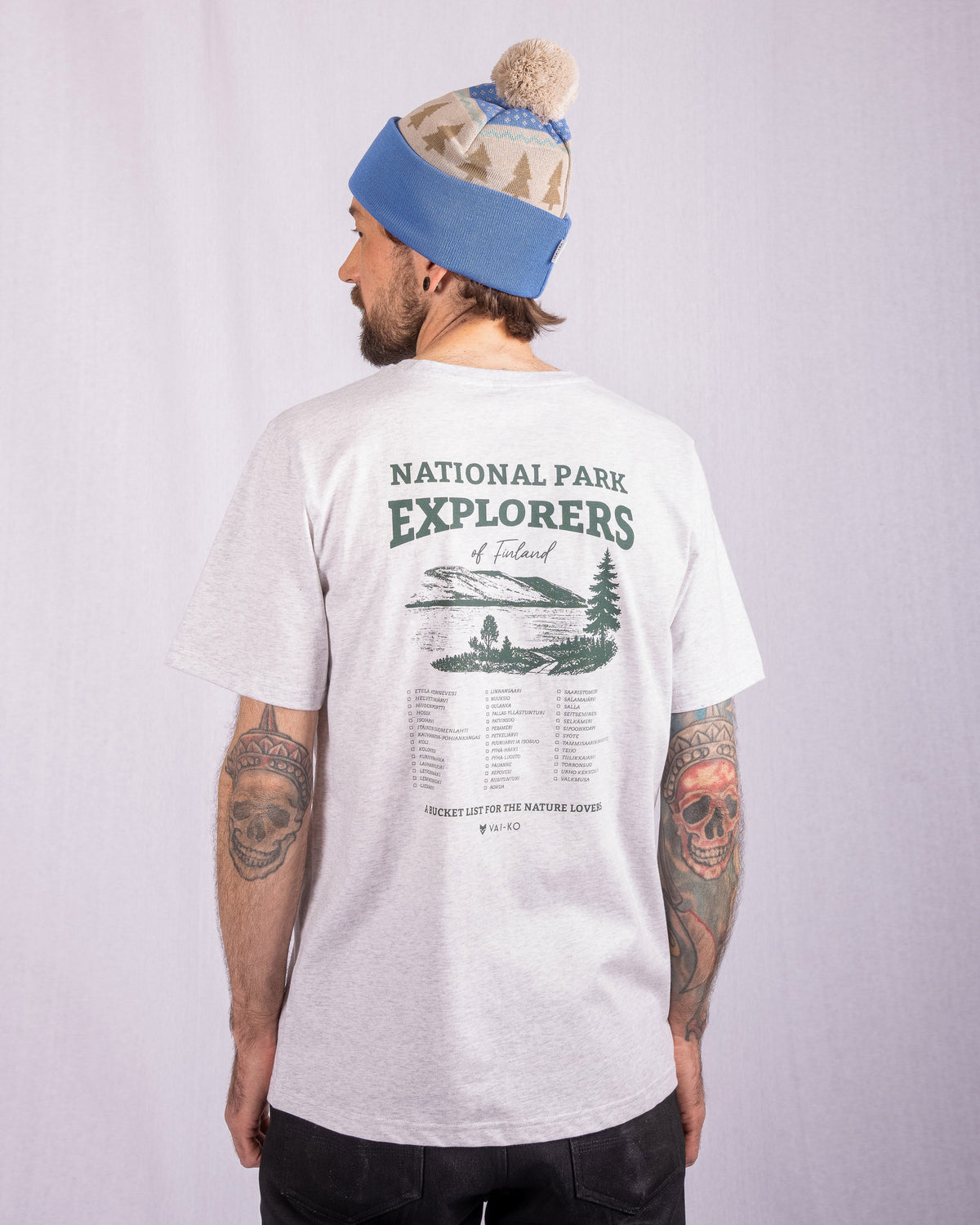 Man in gray National Park Explorers T-shirt and blue beanie, facing away, tattoos on both arms.