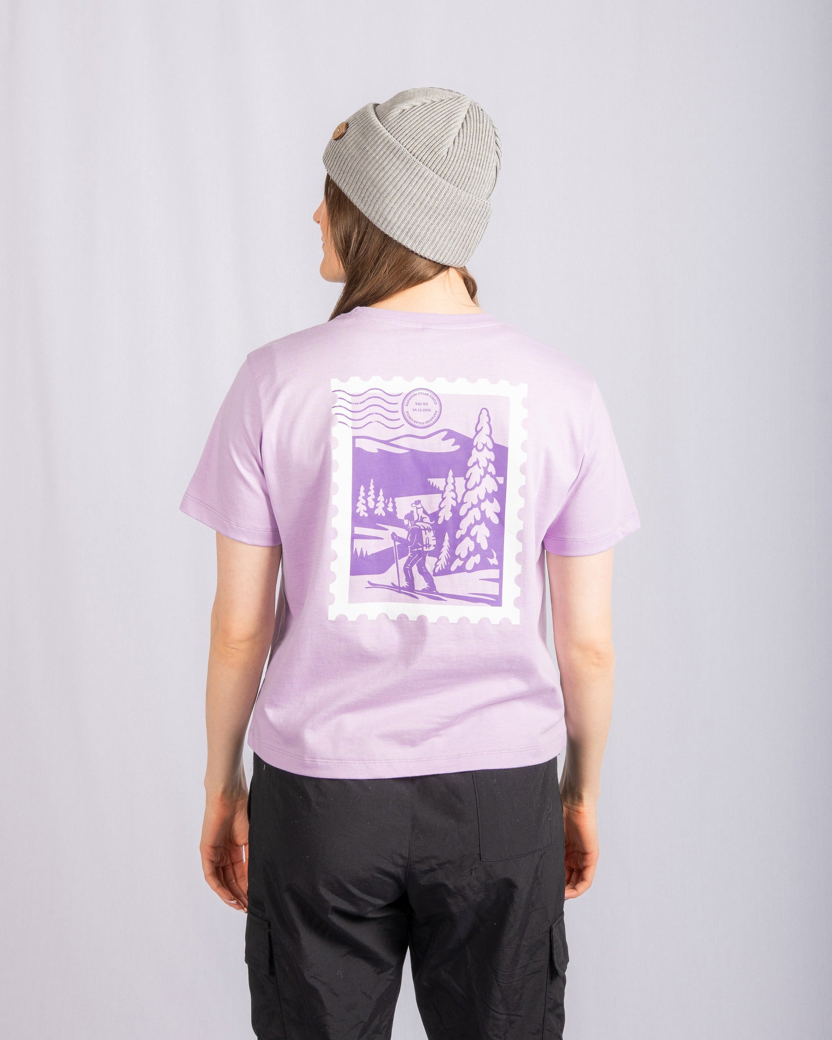 Person wearing a gray beanie and lavender shirt with a purple outdoor scene graphic, standing facing away.