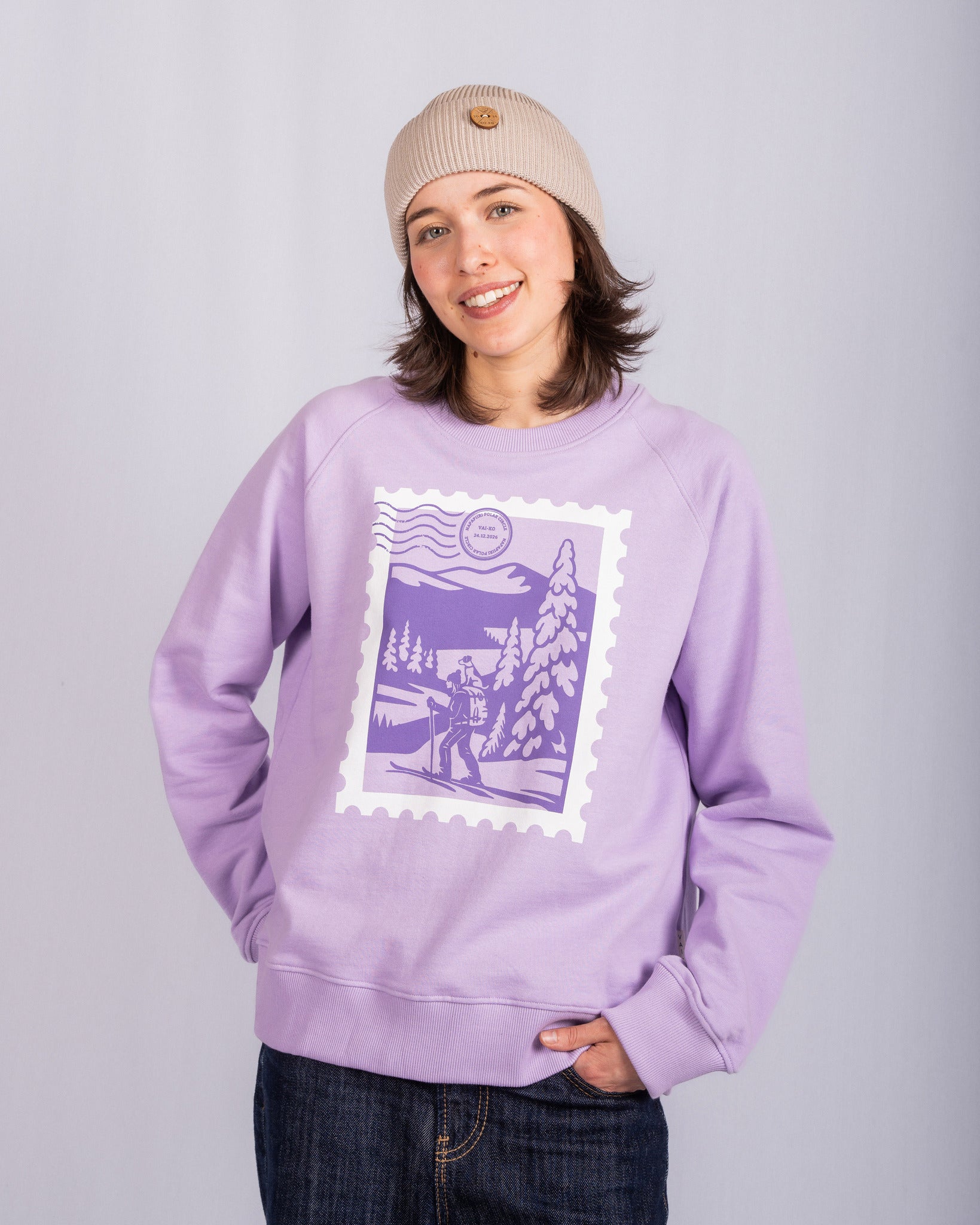 Smiling person in a beige beanie and lavender sweatshirt with a purple winter landscape graphic.