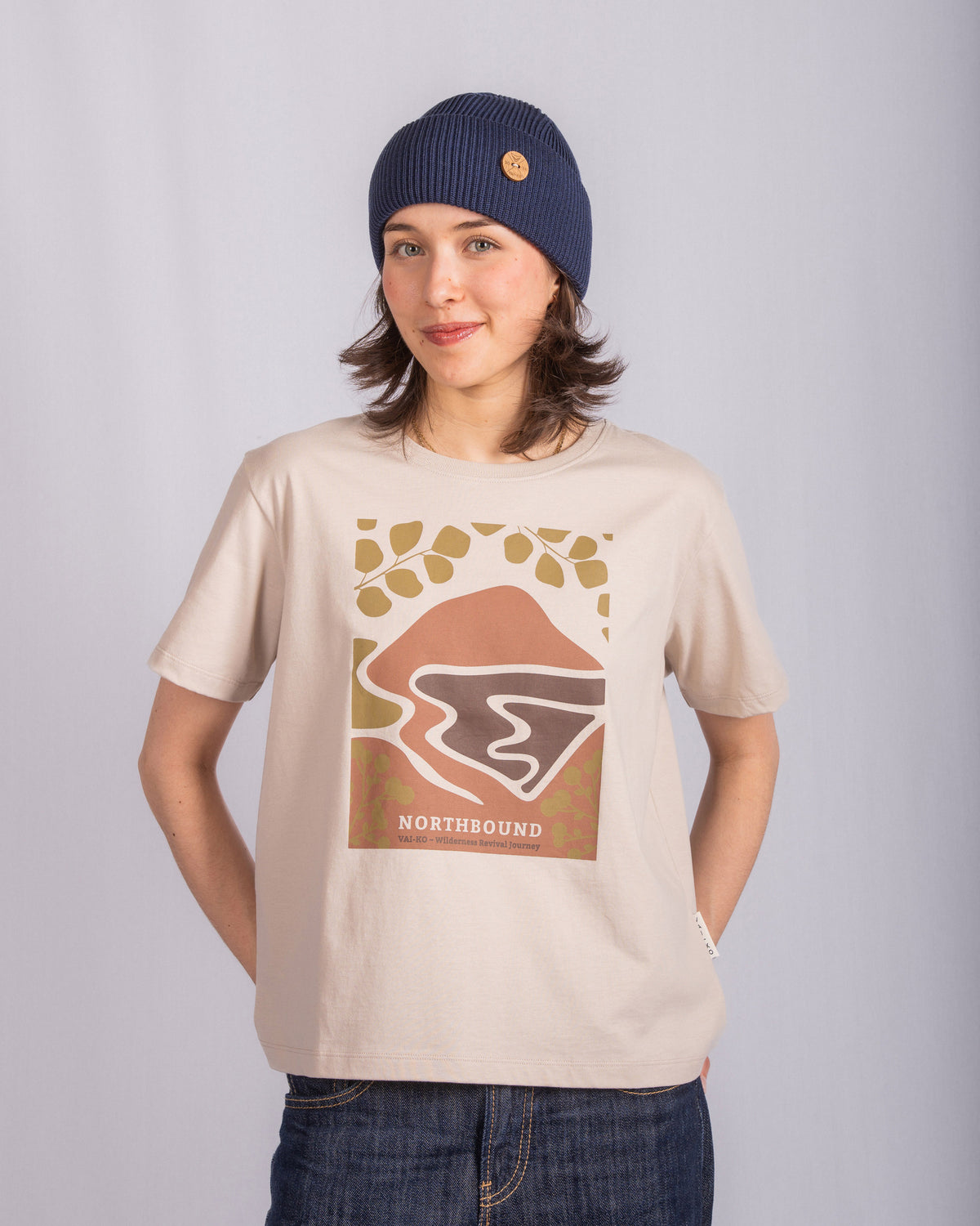 Woman in a blue beanie and graphic NORTHBOUND t-shirt stands against a plain light background.