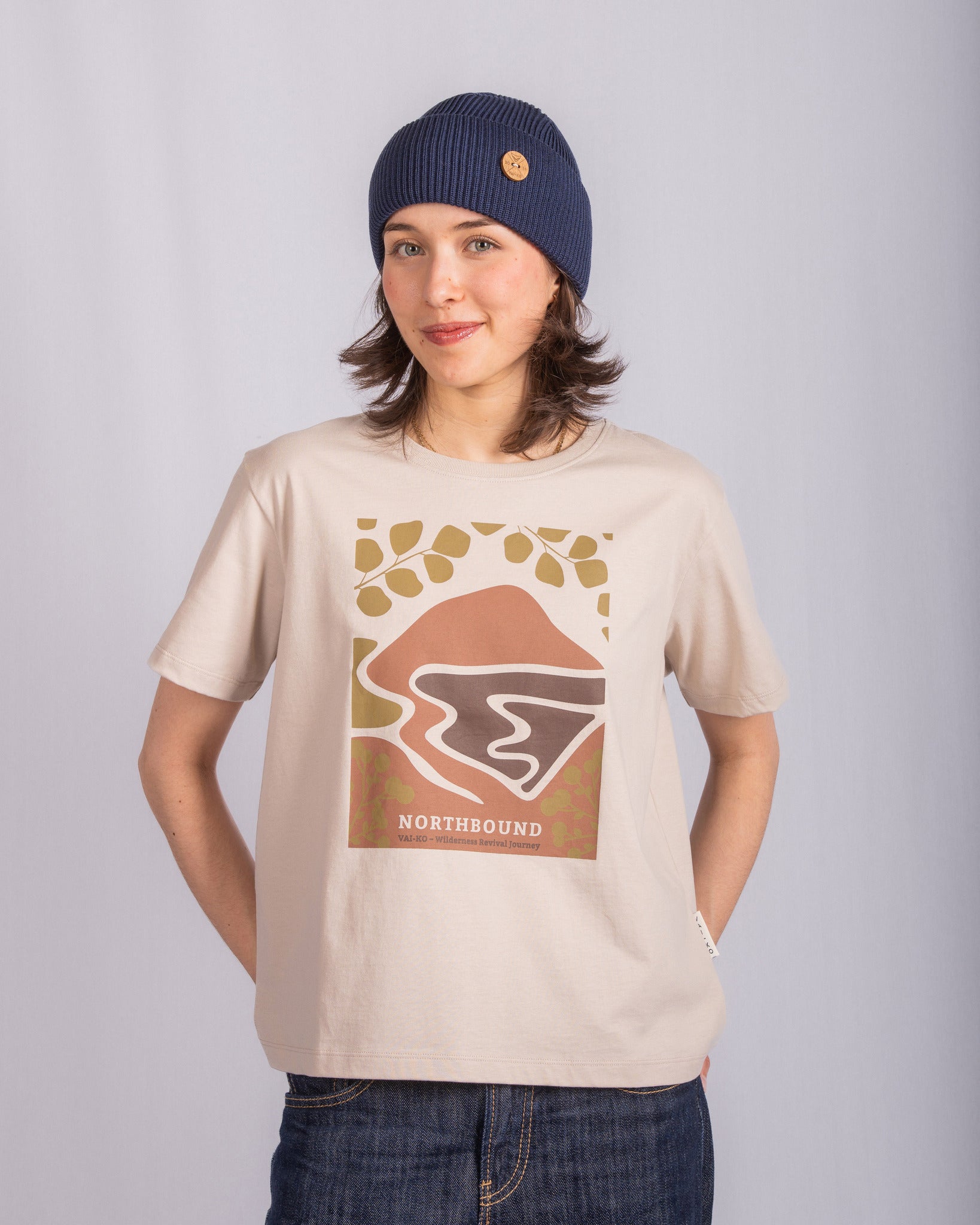 Woman in a blue beanie and graphic NORTHBOUND t-shirt stands against a plain light background.