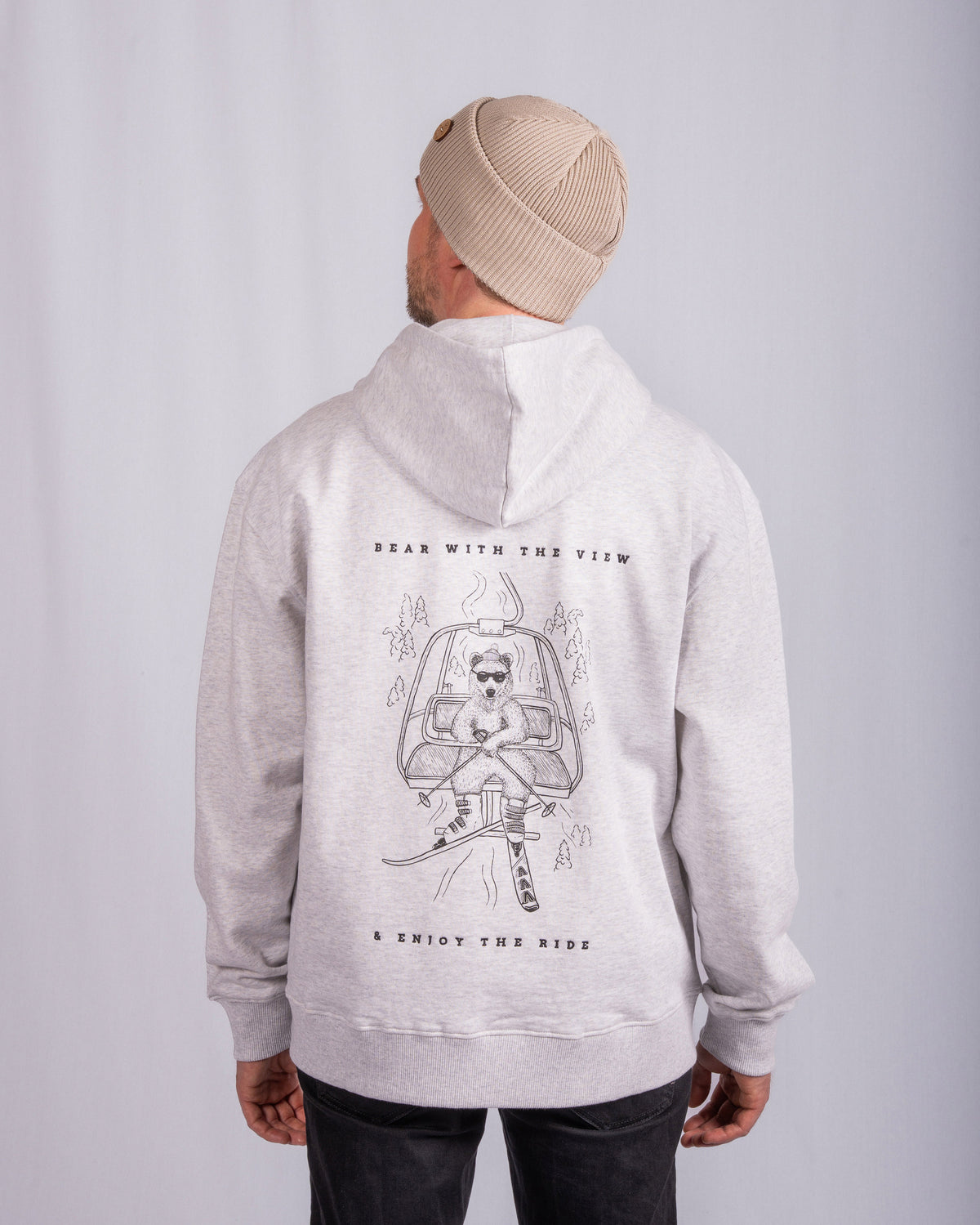 Man in beige beanie and light hoodie with astronaut bear graphic and text Bear with the view & enjoy the ride..