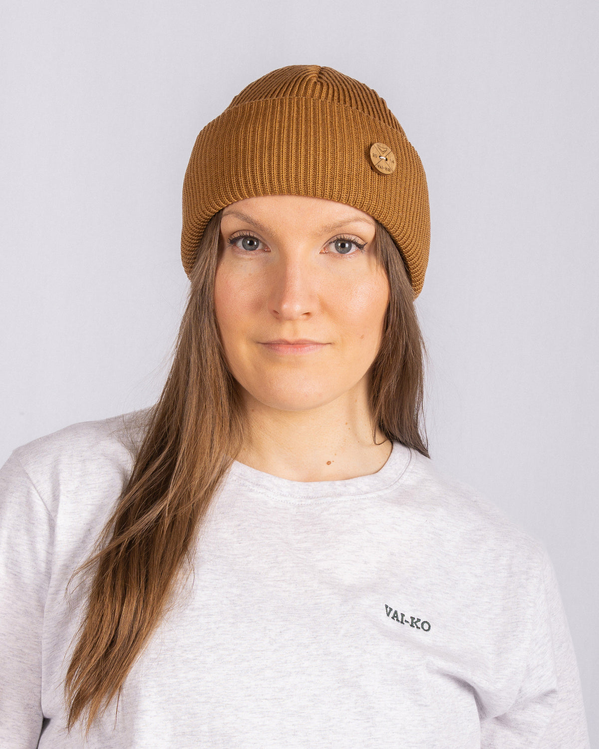 Woman in a brown knit beanie and light grey shirt with VAL-KO text, facing the camera.