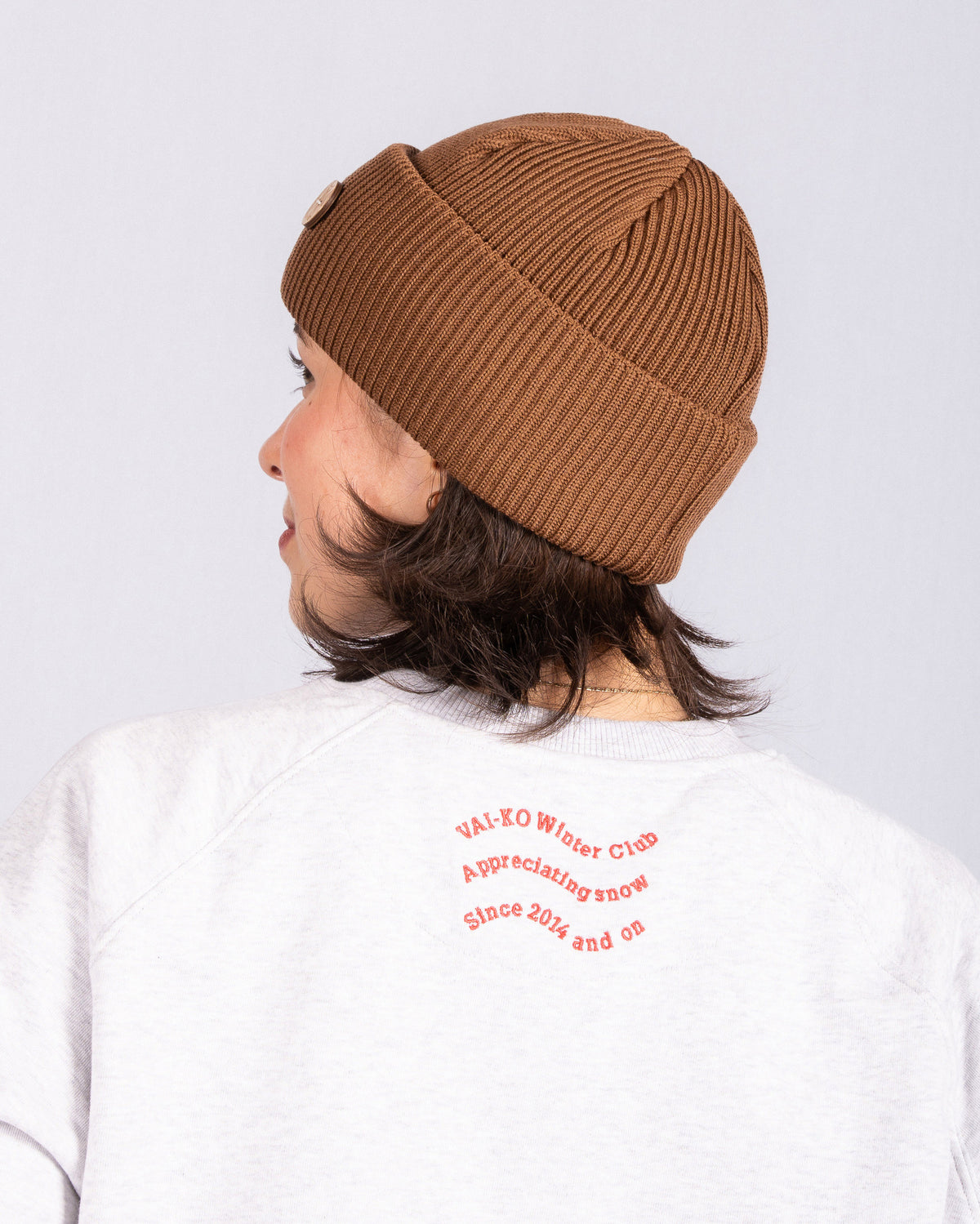Person in a brown beanie and light sweatshirt, text printed on back reads: VAI-KO Winter Club....
