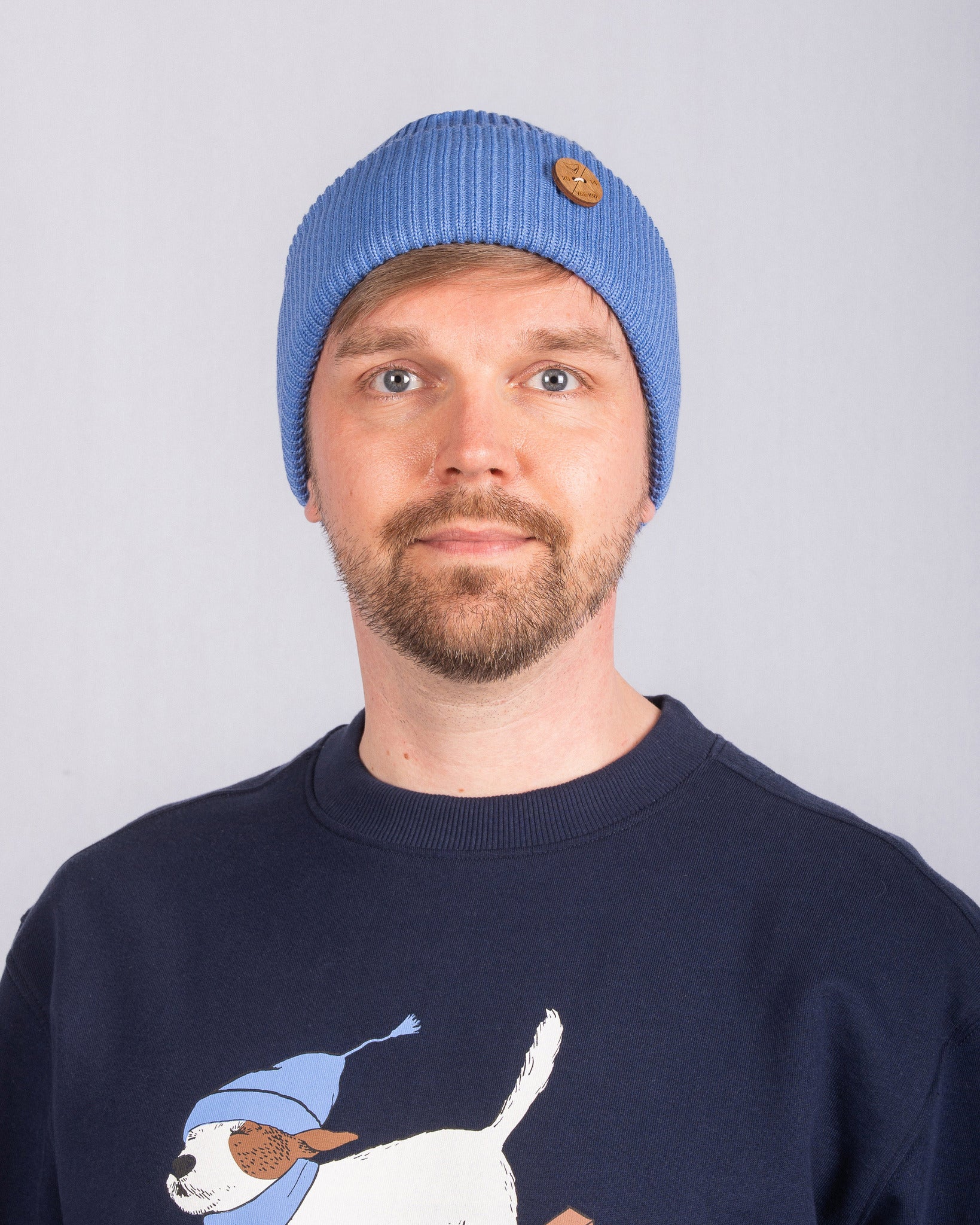 Man with a blue beanie and navy sweater featuring a dog graphic on a plain light background.