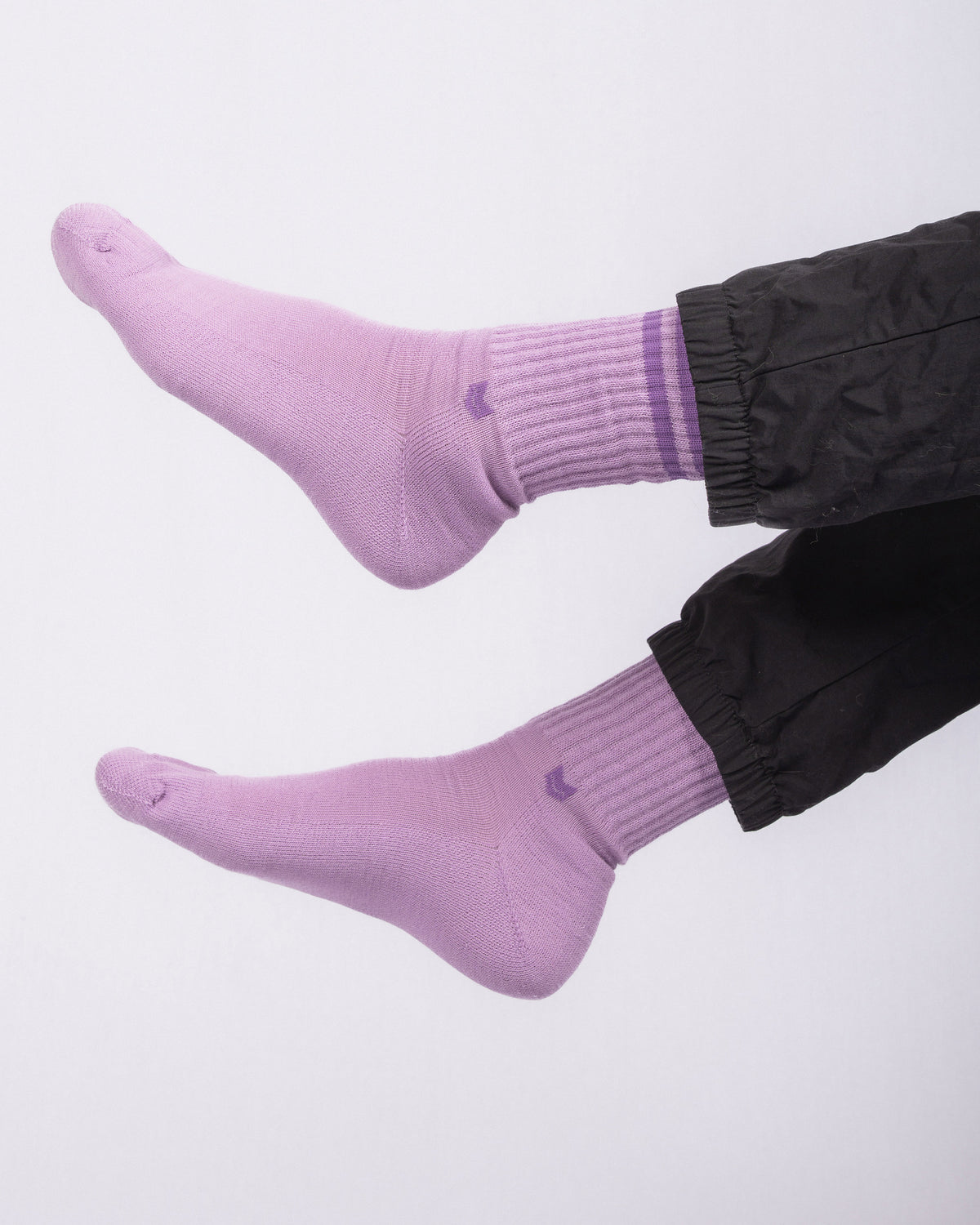 Two feet wearing light purple socks and black pants, raised against a plain white background.